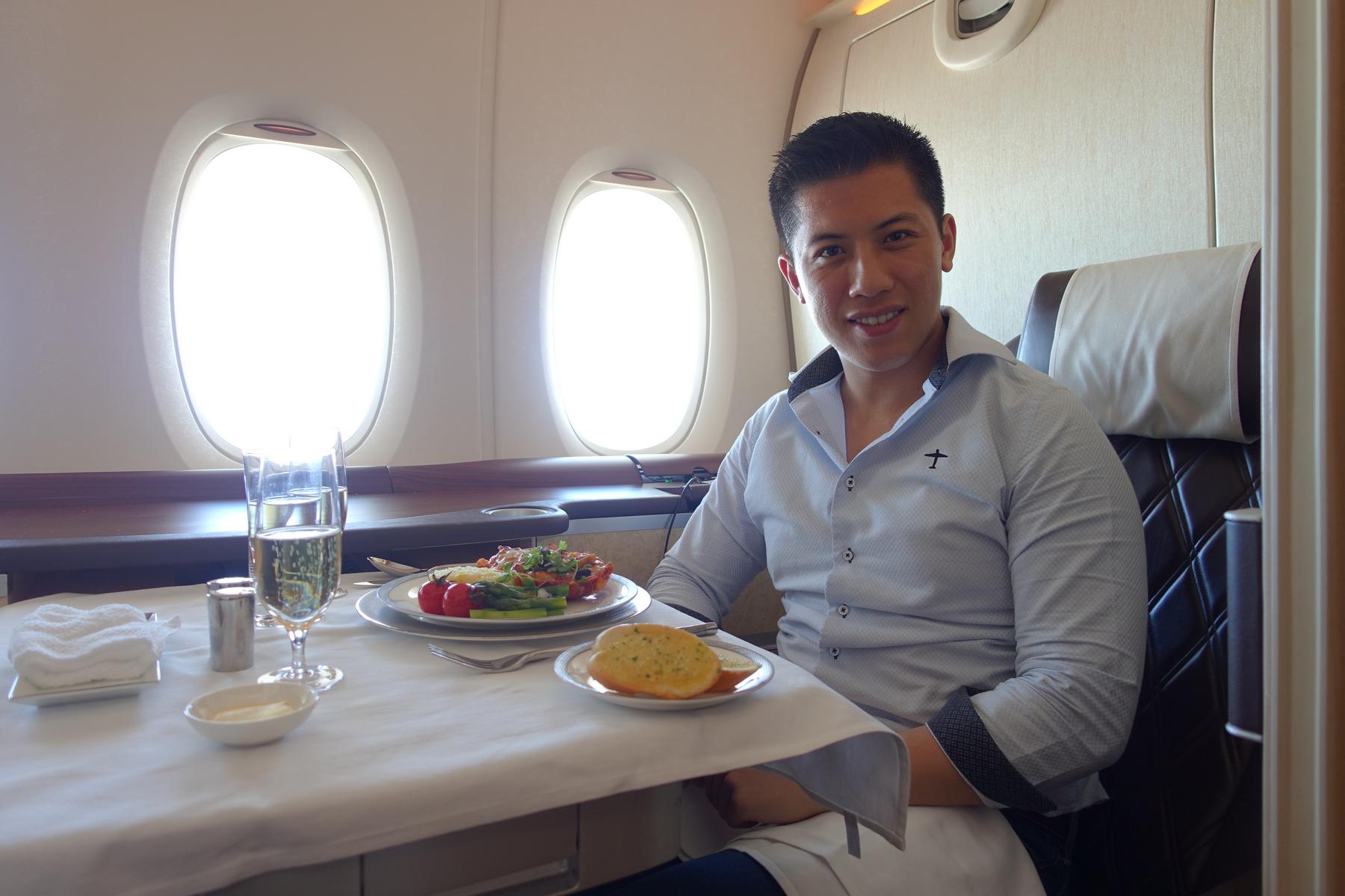 Smiling man having a meal with champagne in a Singapore Airlines A380 First Class suite.