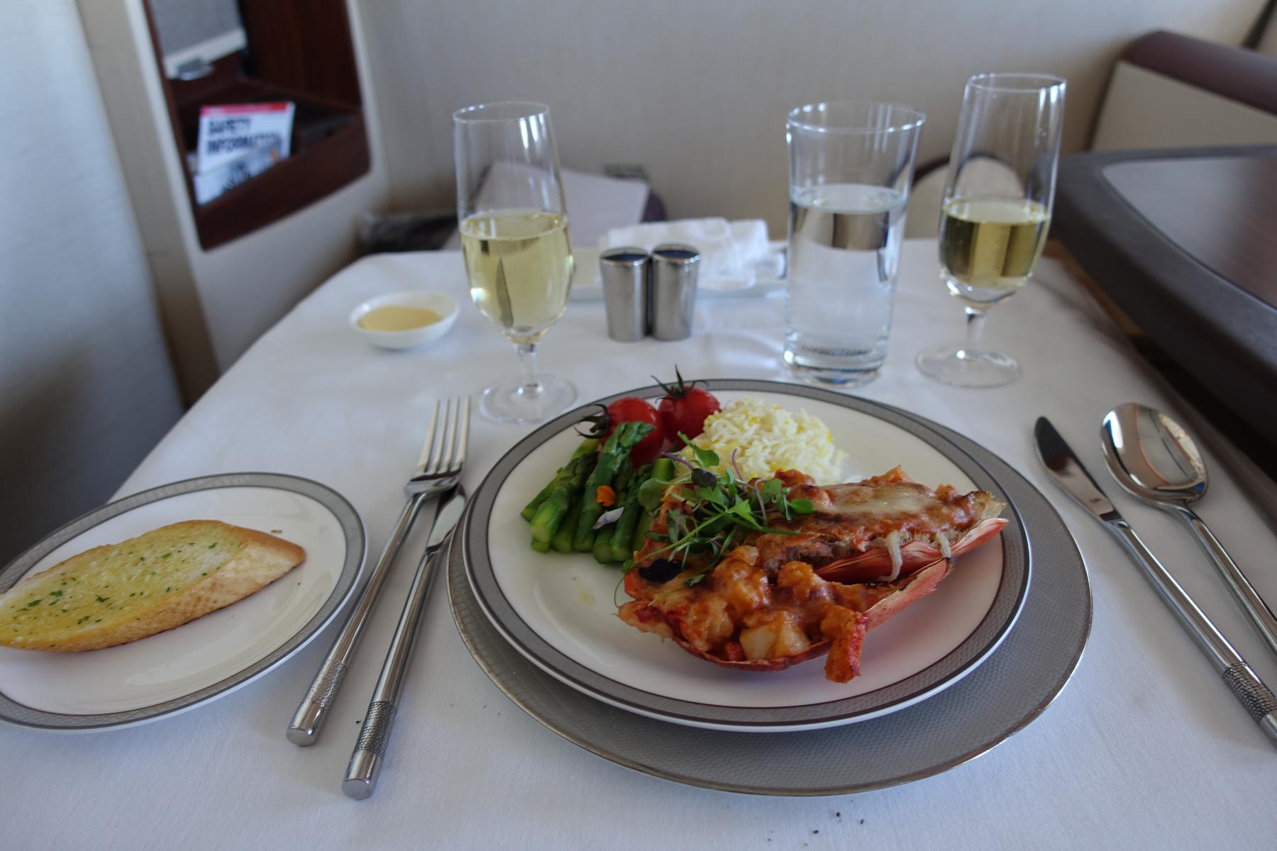 A gourmet lobster meal with champagne, water, and garlic bread served in an airline first class suite.
