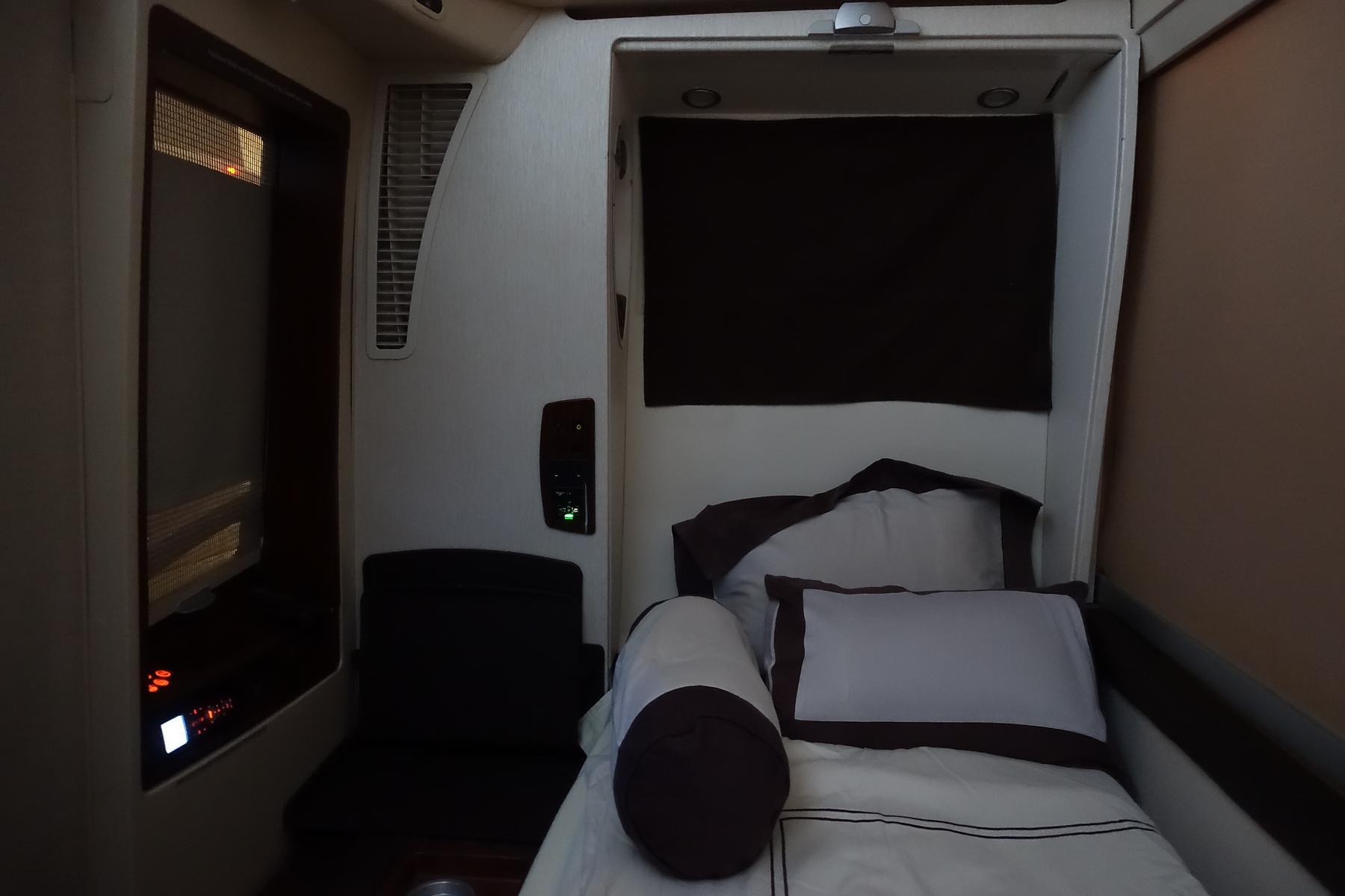 Singapore Airlines A380 First Class Suite with a made-up bed, a small seat, and a window with a shade.