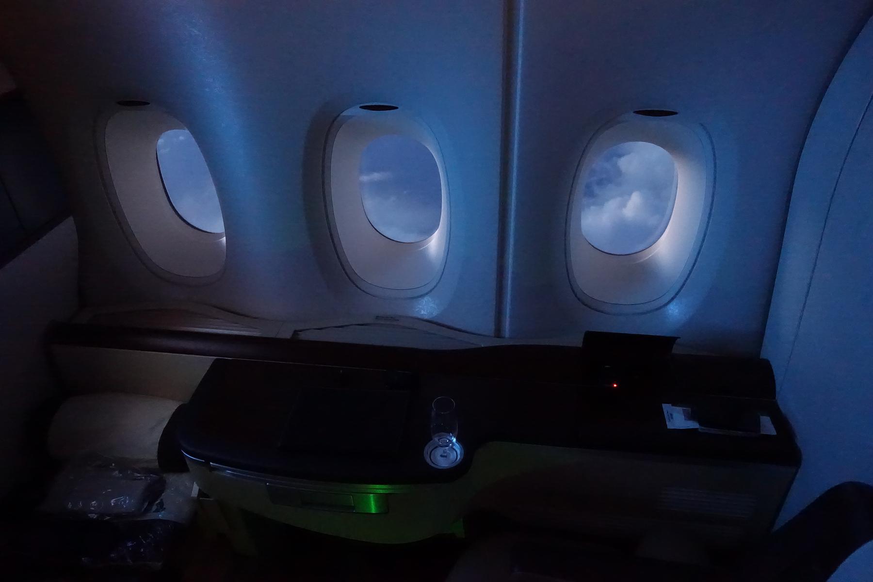 Dark interior of a Singapore Airlines First Class Suite with three windows showing clouds.
