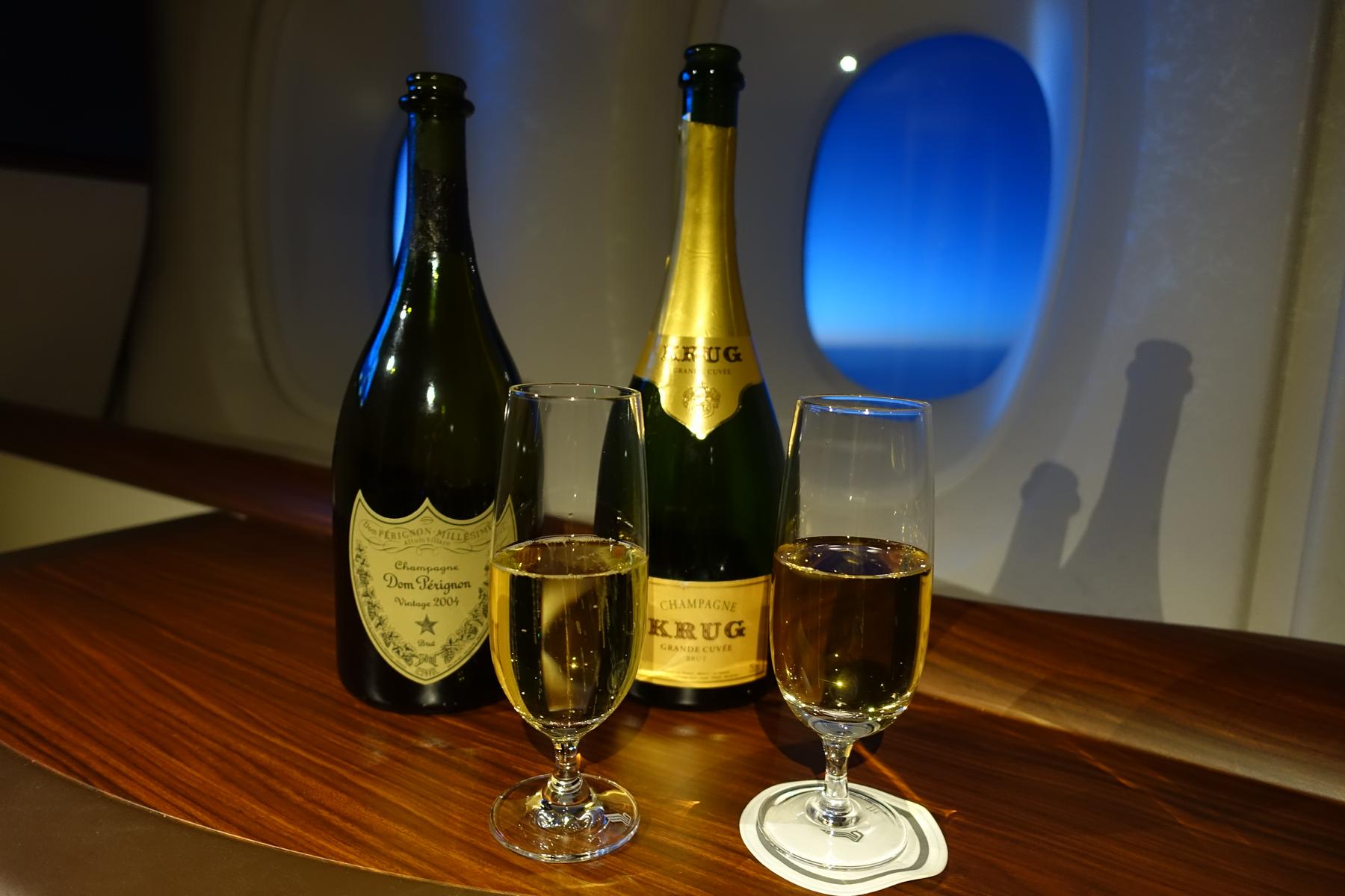 Two bottles of champagne and two full glasses on a wooden table in an airplane suite.