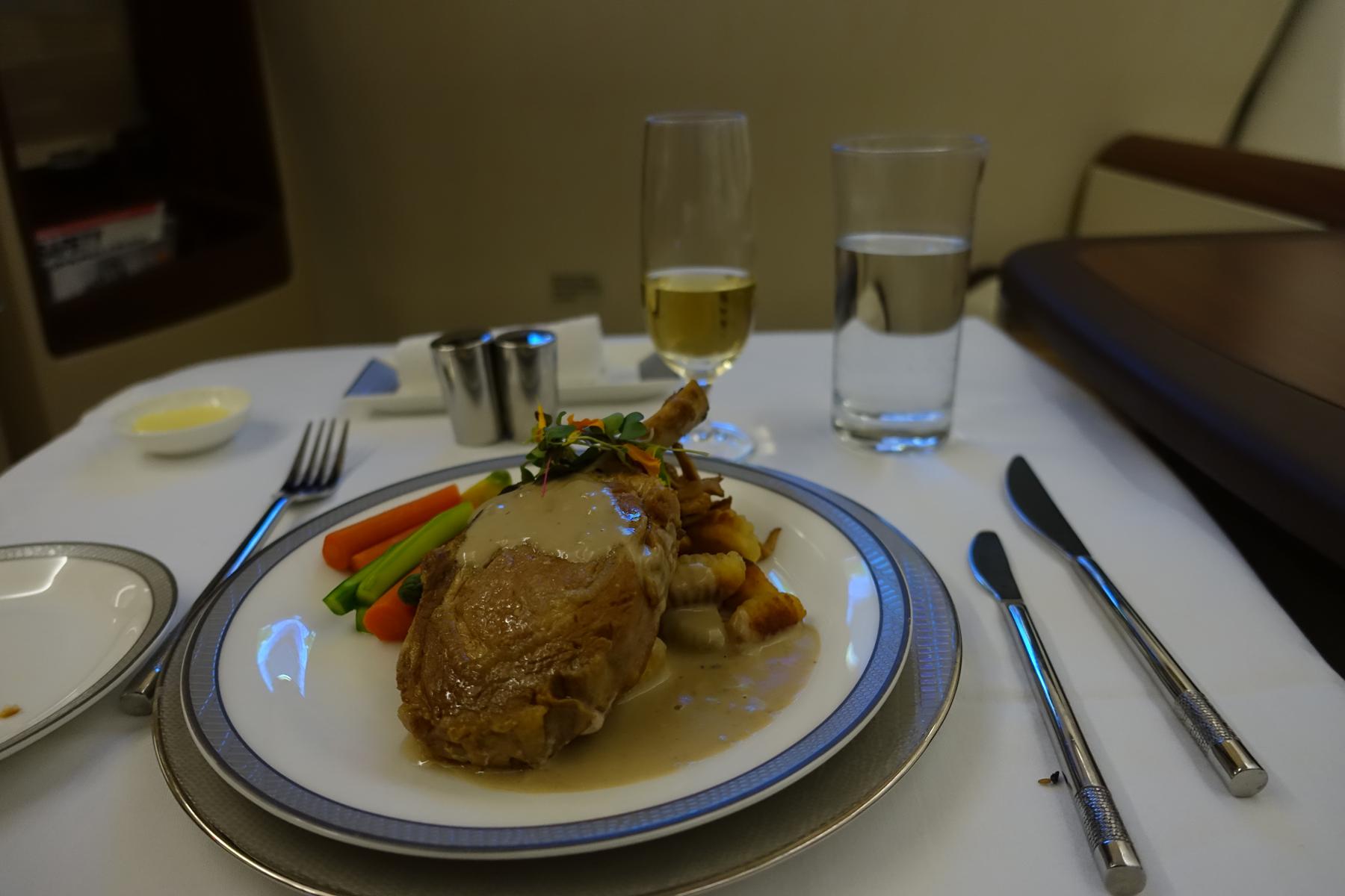 An elegant meal with a main course, vegetables, wine, and water served in a Singapore Airlines First Class suite.