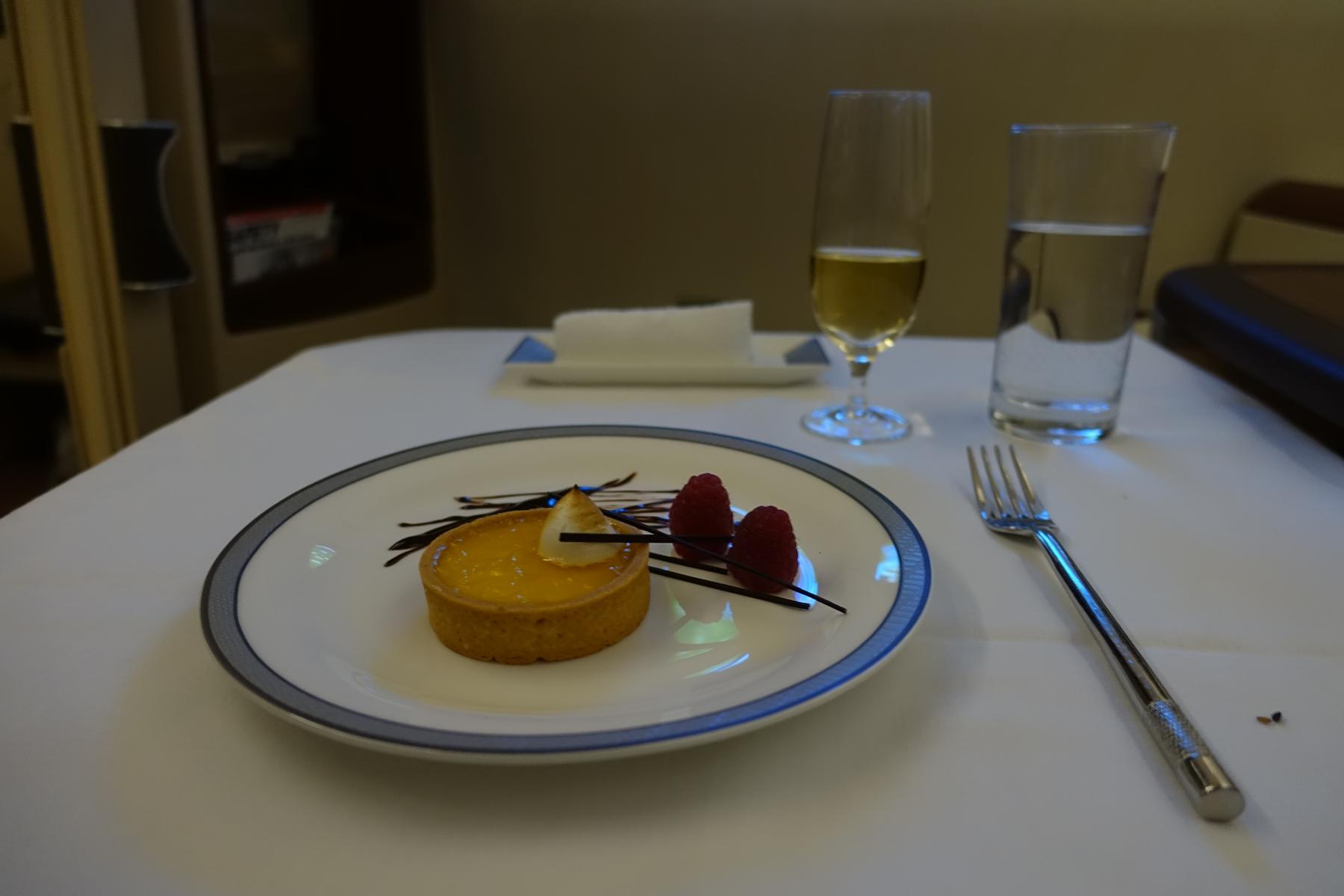 A plated dessert of a tart with raspberries and champagne on a white table in Singapore Airlines First Class.