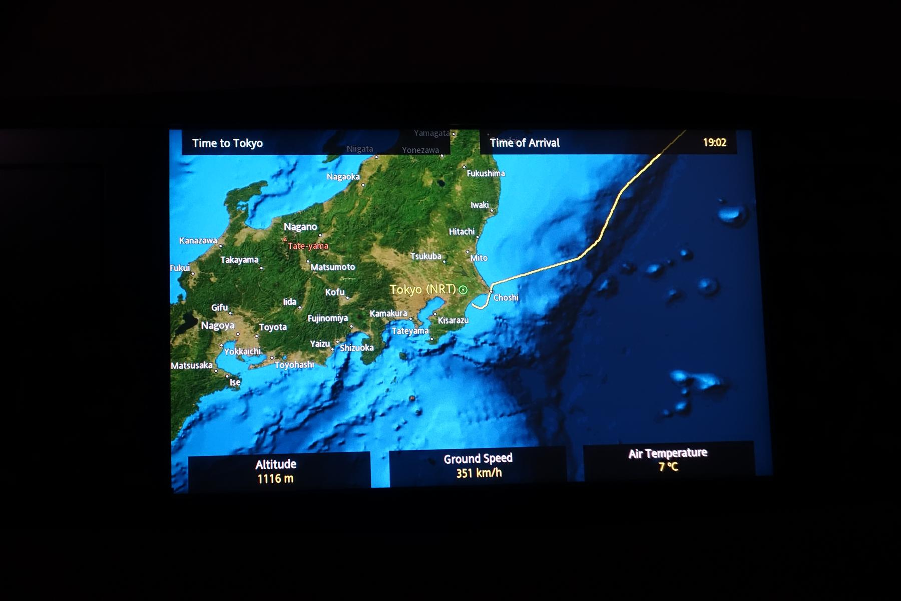 An in-flight entertainment screen displays a map of Japan with the flight path approaching Tokyo and current flight data.