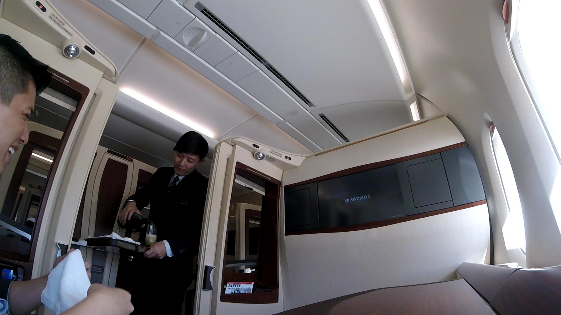 A flight attendant pours a drink for a passenger in a Singapore Airlines First Class suite.
