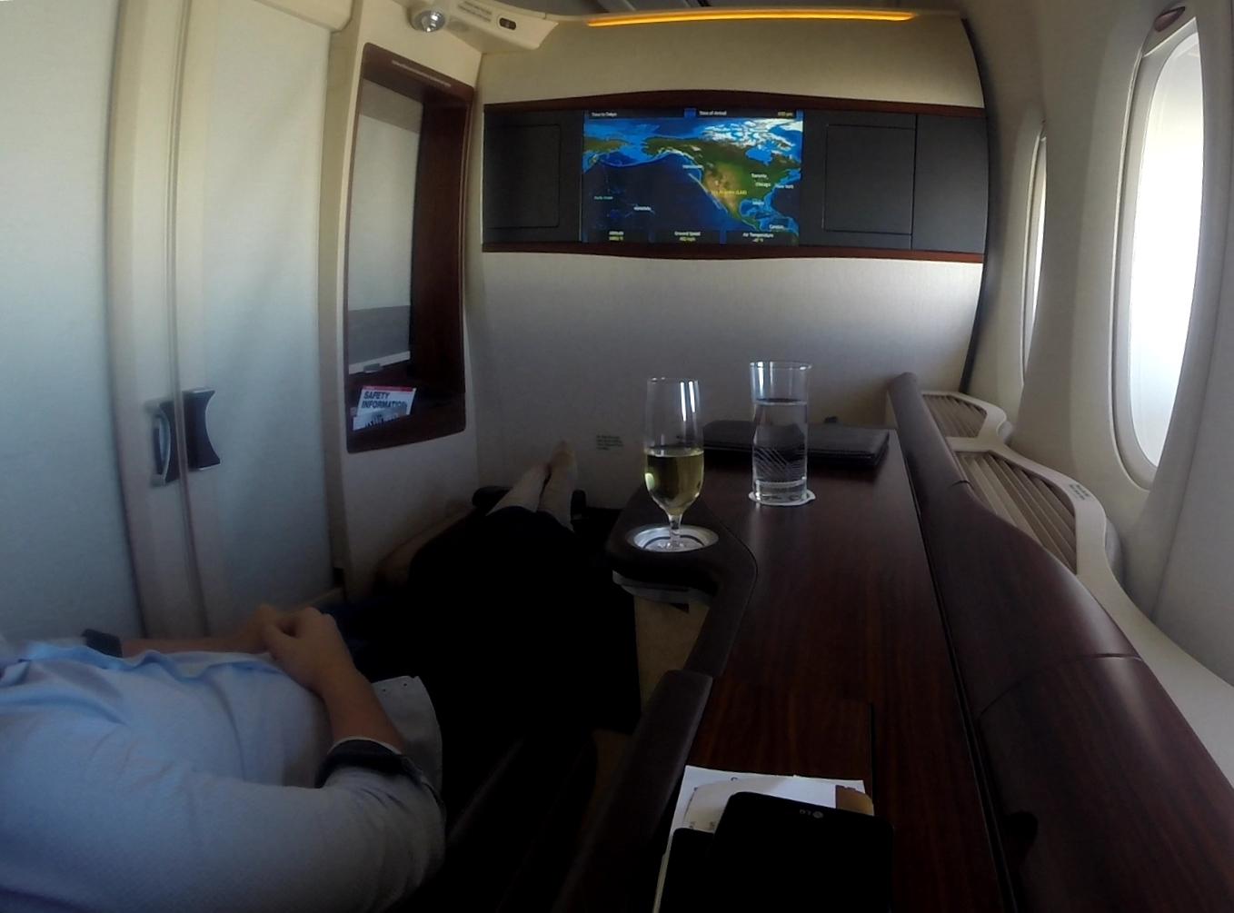 A person relaxing in a luxurious Singapore Airlines A380 First Class suite with a flight map on screen and champagne on the table.