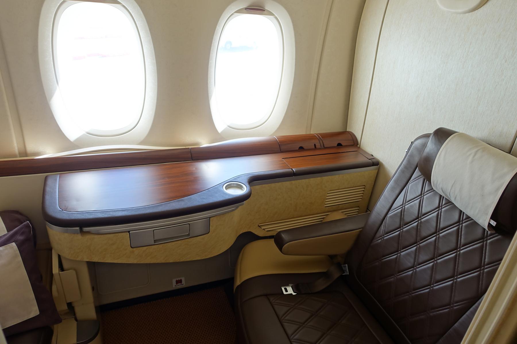 A Singapore Airlines First Class A380 suite with a brown quilted leather seat, wooden counter, and two windows.