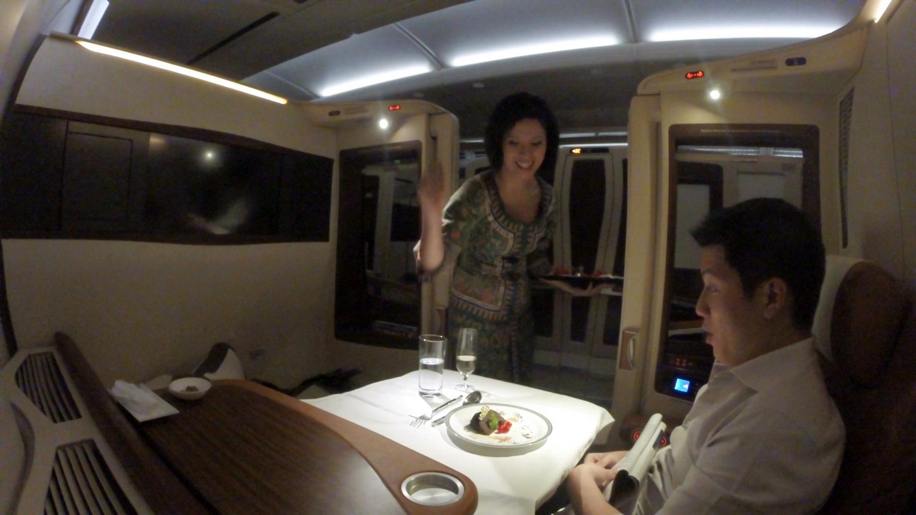 Flight attendant serving dessert to a man in a Singapore Airlines First Class suite.