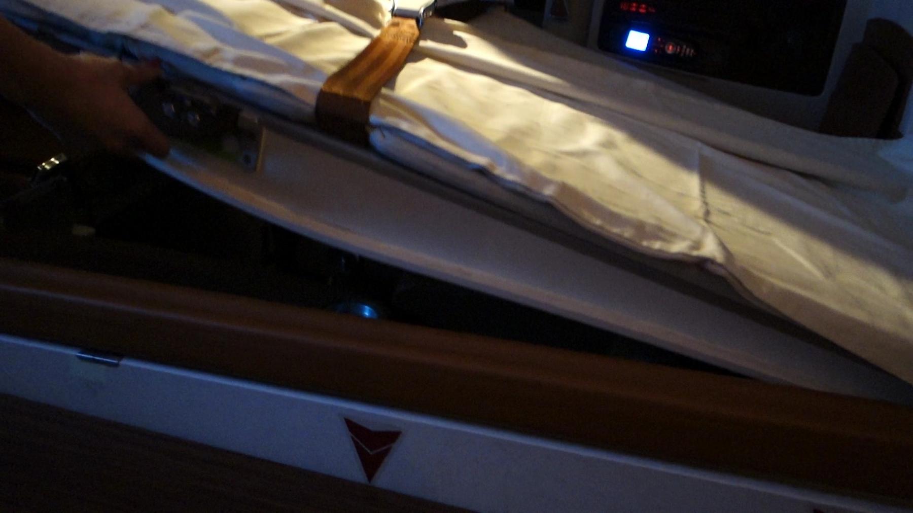 A hand adjusting a white-sheeted bed with a seatbelt in a Singapore Airlines First Class Suite.