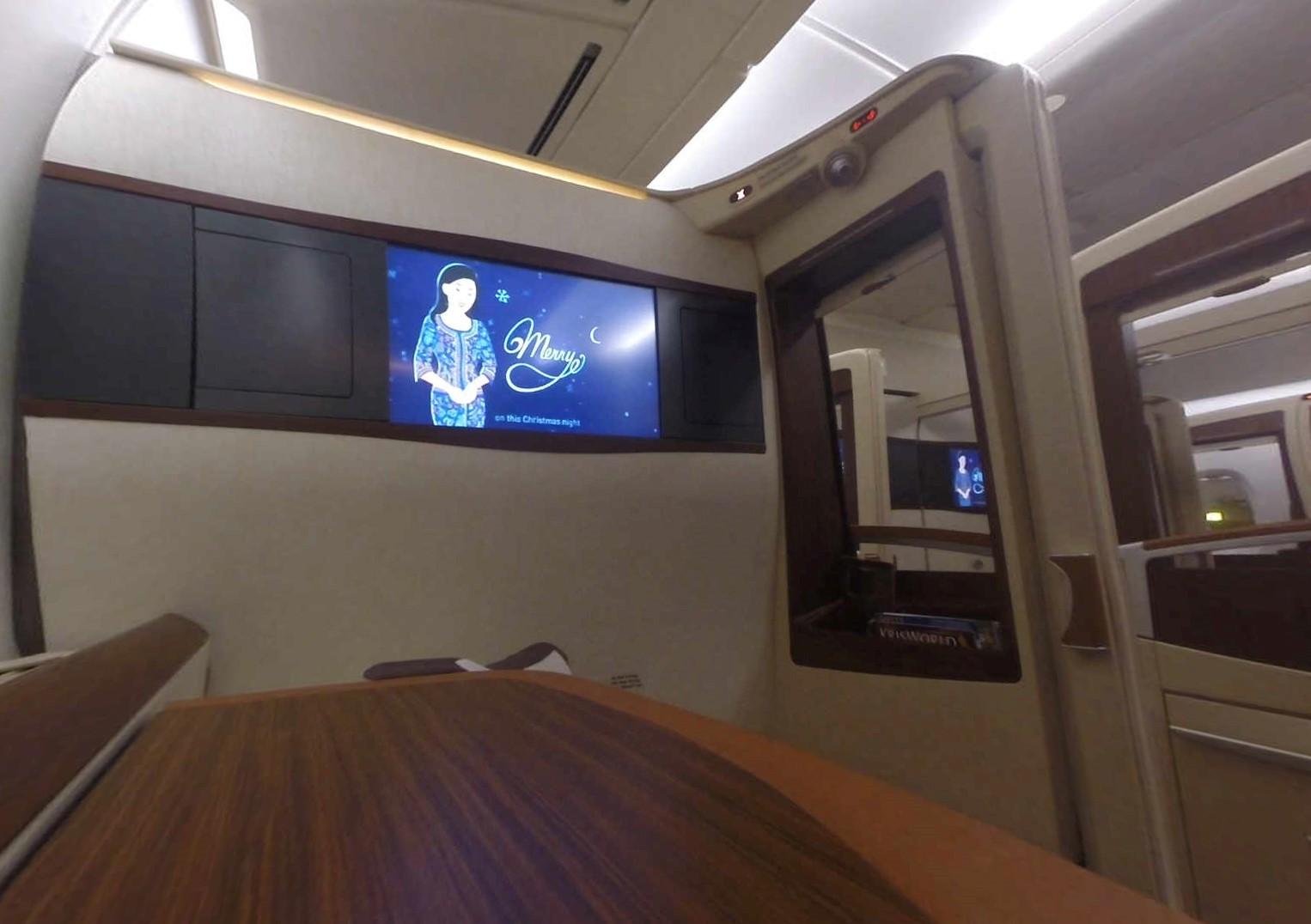 Inside a private Singapore Airlines First Class Suite, a large screen displays a Merry Christmas message.