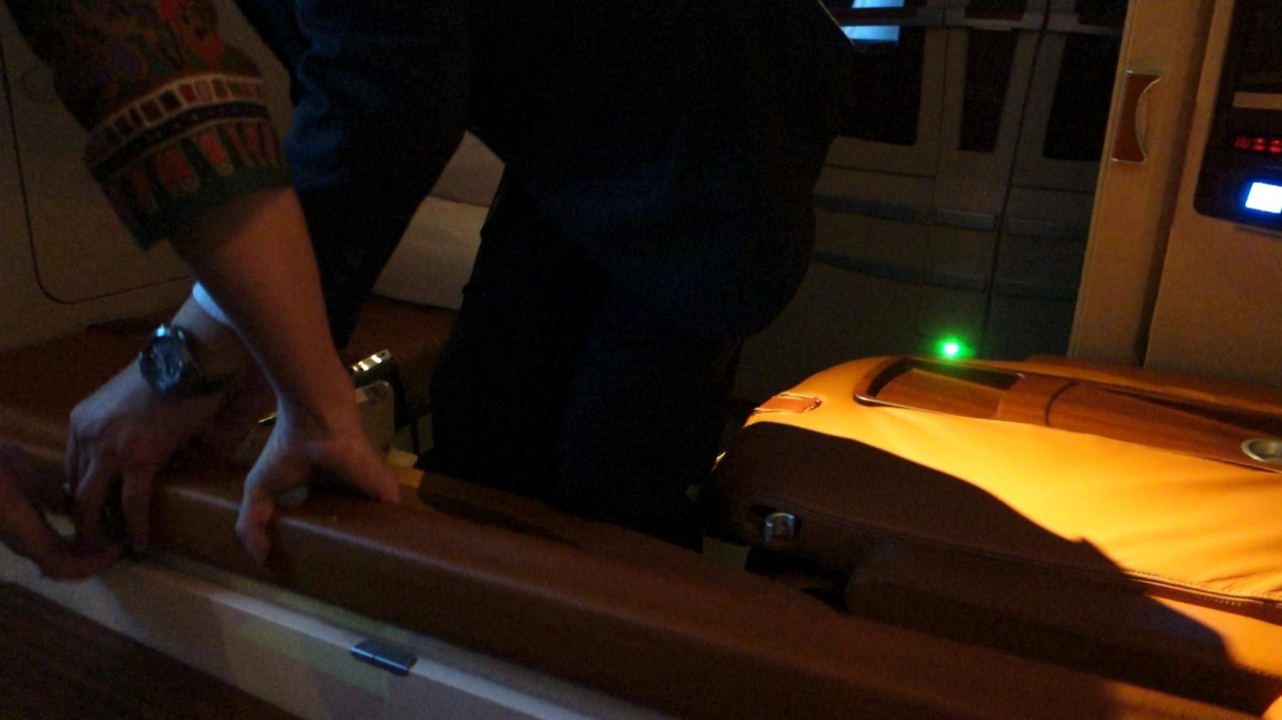 A person's hands with a watch and patterned sleeve rest on the elegant brown leather interior of a Singapore Airlines First Class suite.