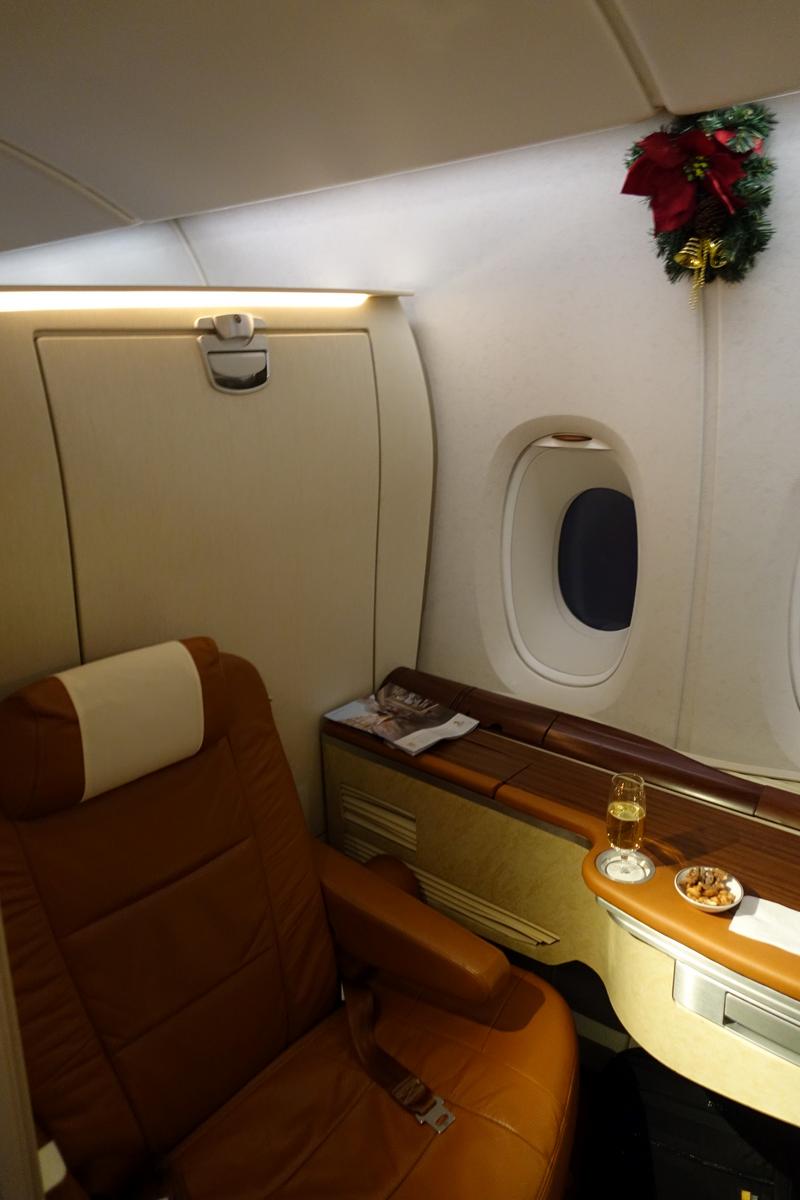 A luxurious airplane first-class suite with a brown leather seat, window, champagne, and a Christmas decoration.