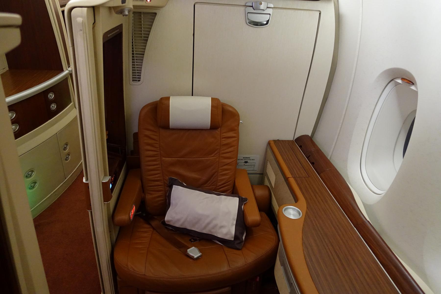 Singapore Airlines First Class Suite with a brown leather seat, side table, and window.