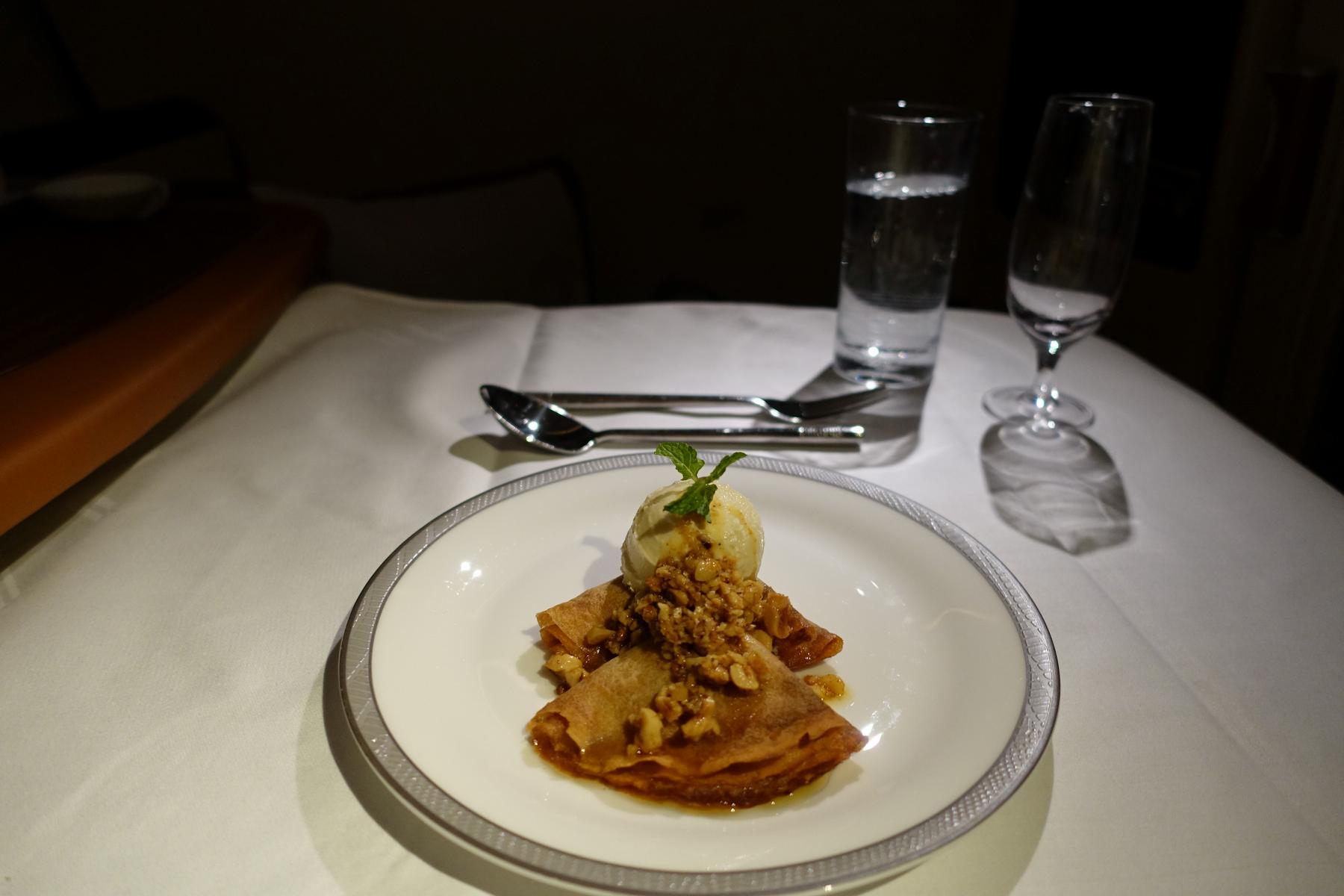 An elegant dessert of crepes with ice cream, nuts, and a mint leaf is served on a white tablecloth.