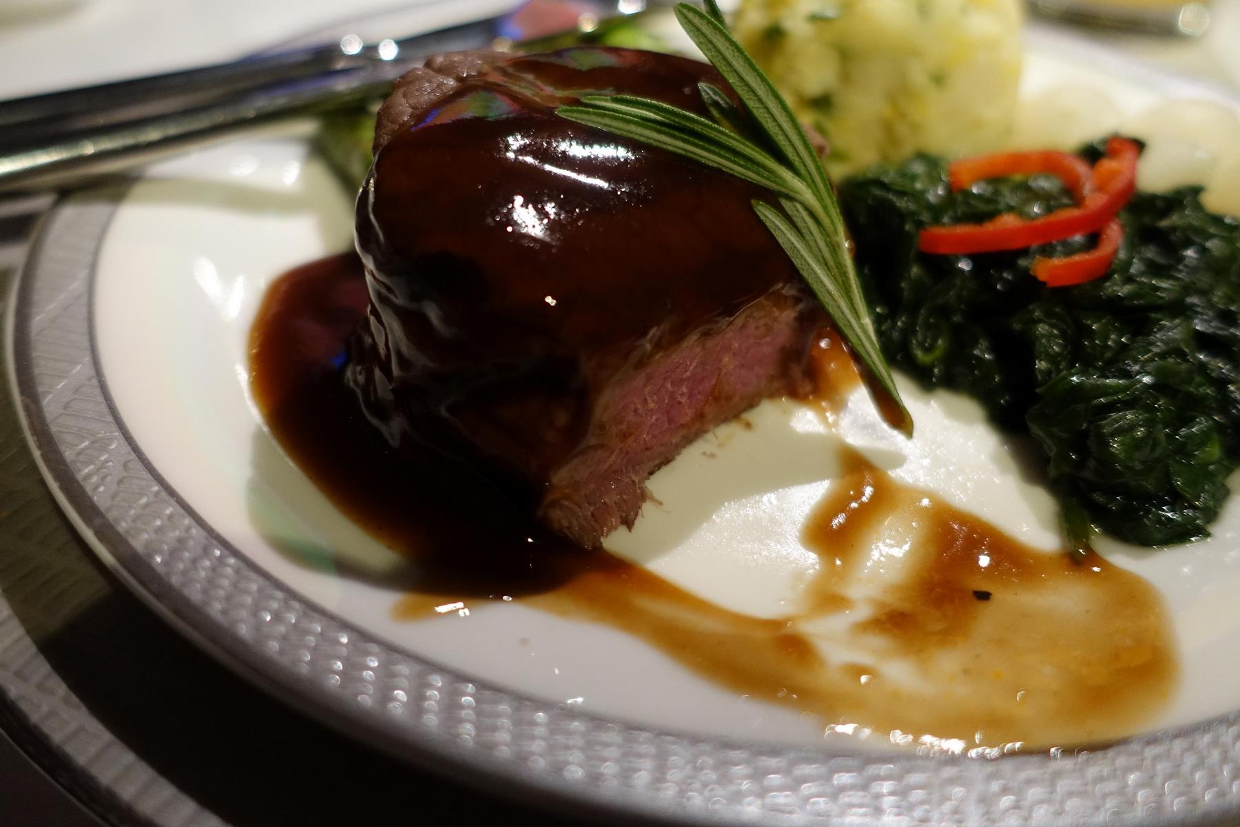 Gourmet steak with dark sauce and rosemary served on a Singapore Airlines First Class plate.
