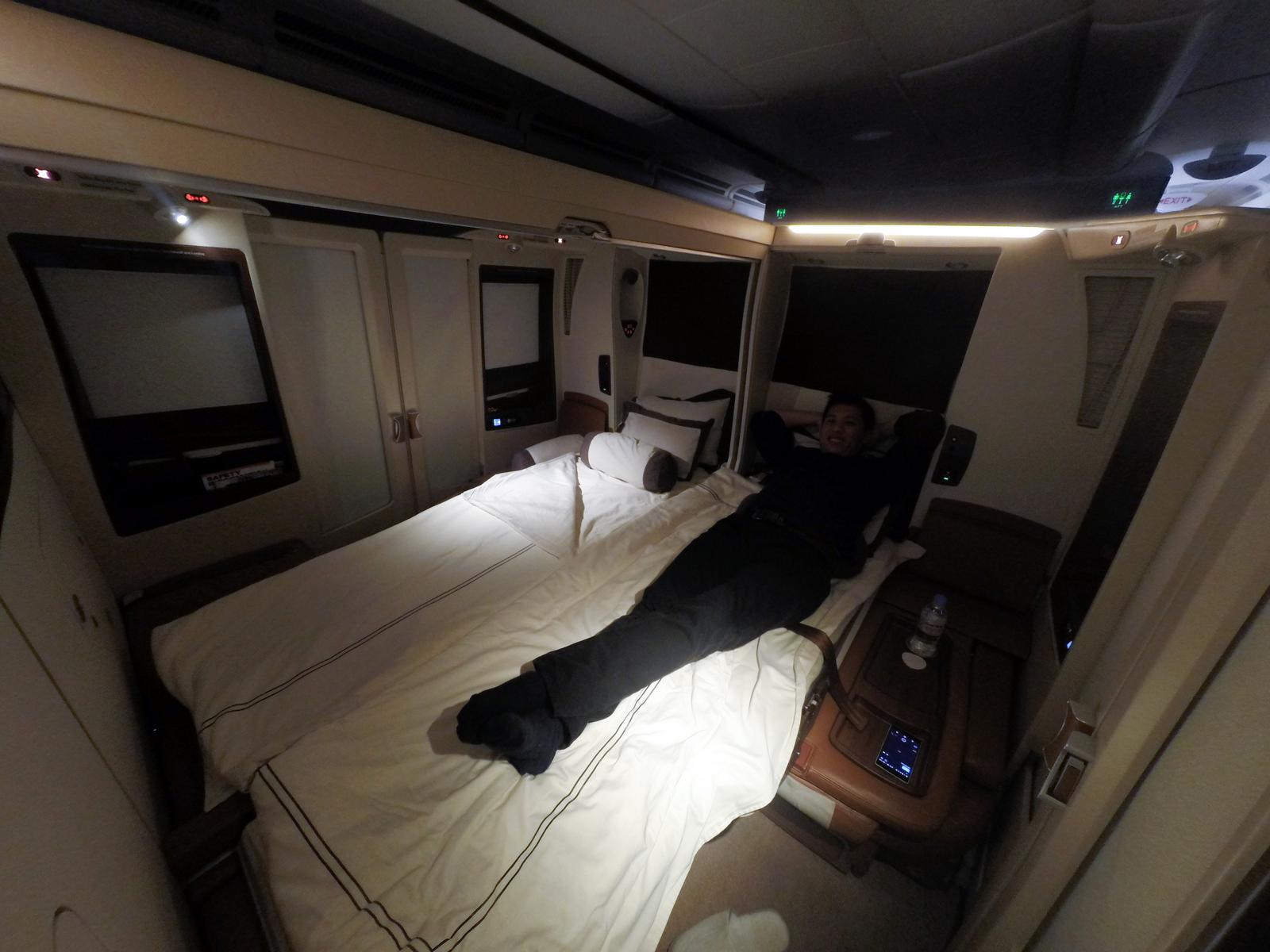 A man smiles while relaxing on a large bed in a Singapore Airlines First Class Suite.