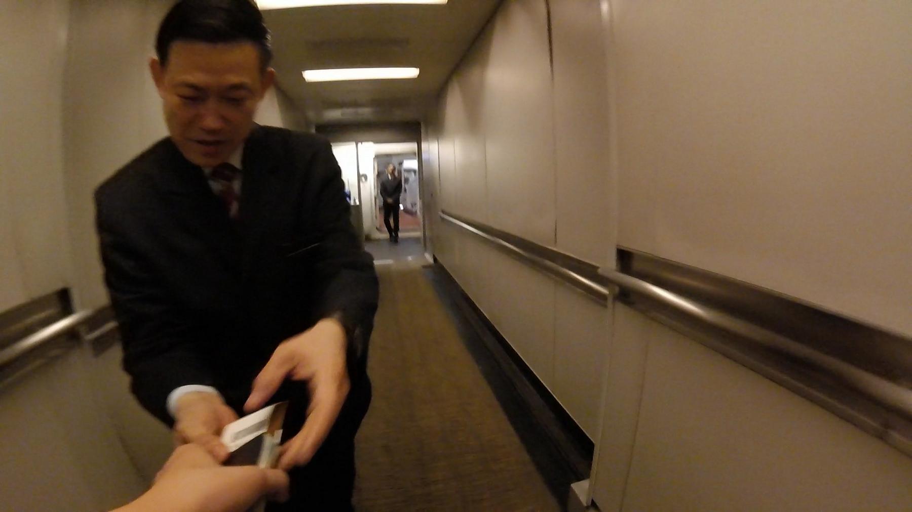 An airline staff member hands a document to a passenger in an airport jet bridge.
