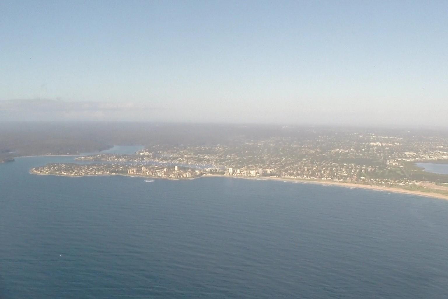 Aerial view of a hazy coastal city with beaches and ocean.