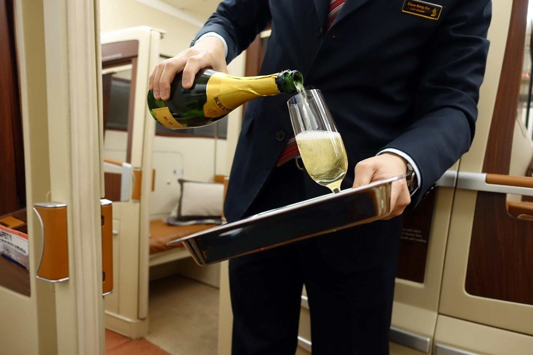 A flight attendant pours Krug champagne into a glass inside a Singapore Airlines First Class Suite.