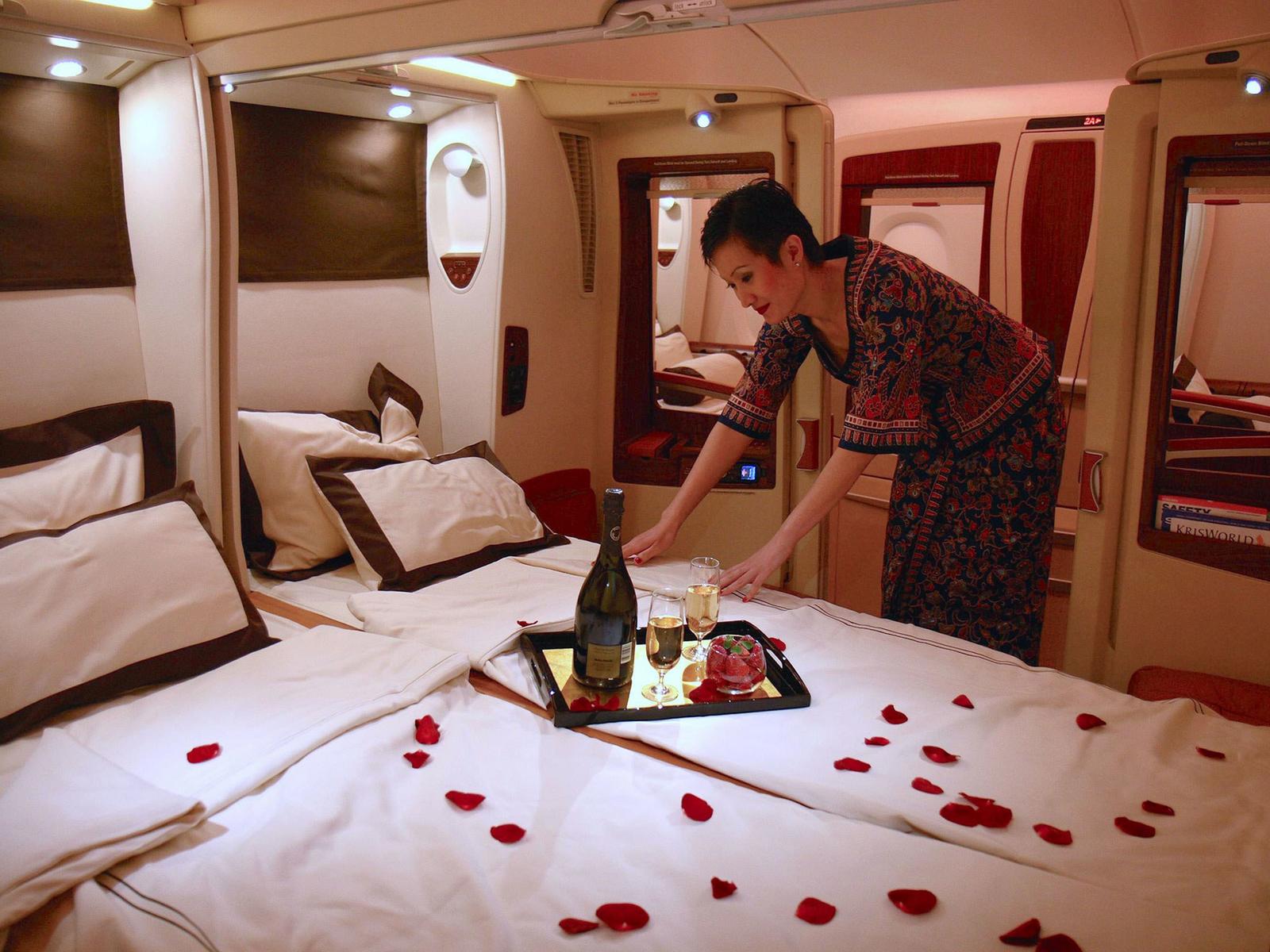 A Singapore Airlines flight attendant prepares a bed with champagne, strawberries, and rose petals in a luxurious First Class Suite.