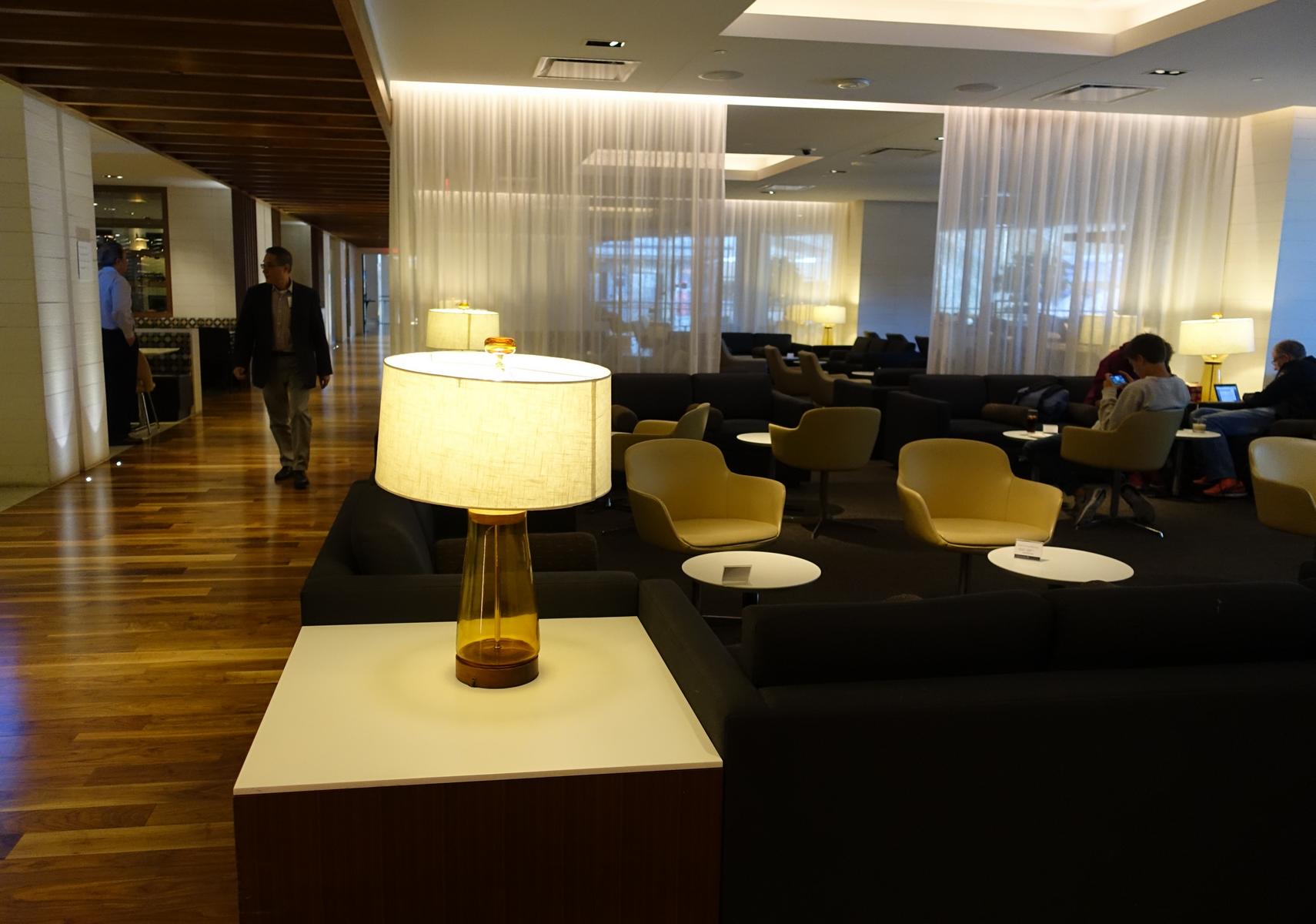 The spacious, modern Star Alliance Lounge at LAX, featuring dark sofas, yellow armchairs, ambient lighting, and a few guests.