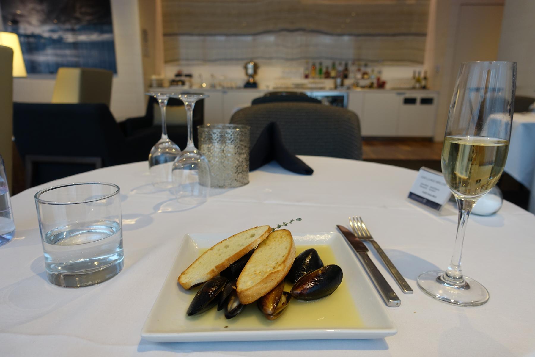 A plate of mussels with bread and a glass of champagne on a table in the Star Alliance First Class Lounge.