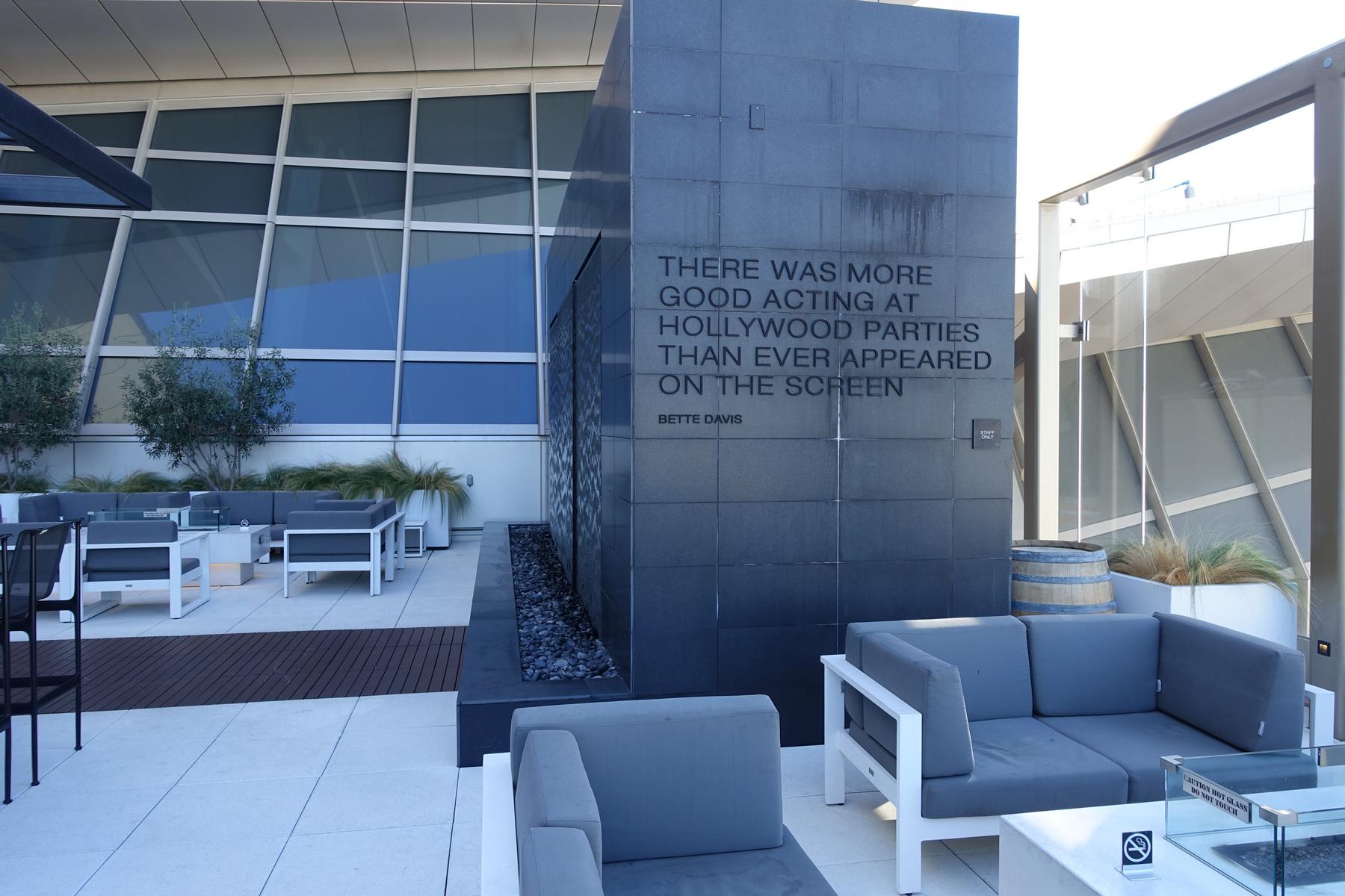 An outdoor lounge patio with modern seating and a stone wall featuring a Bette Davis quote.
