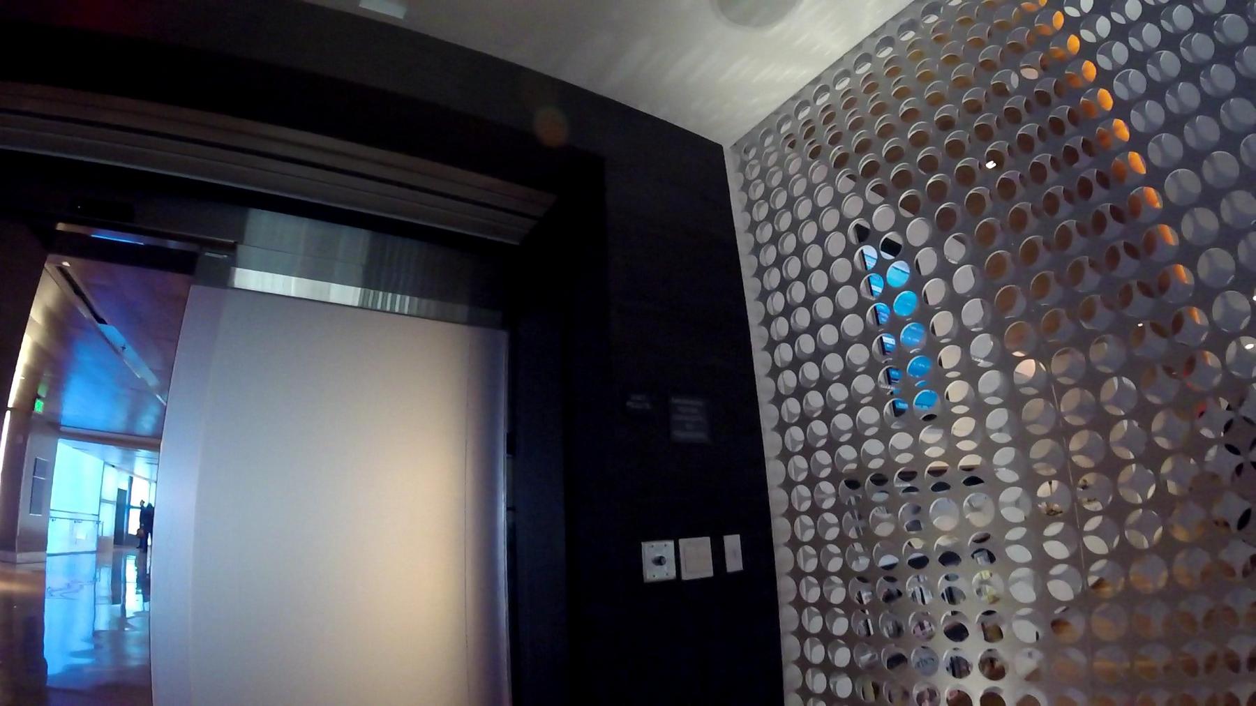 An entrance to a modern airport lounge with a perforated metal screen and a blue-lit hallway.