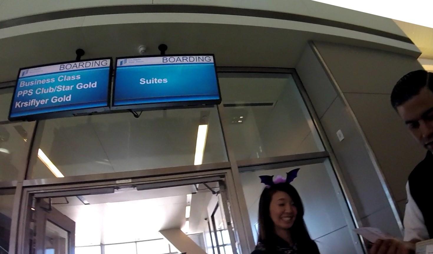 Boarding screens for Business Class and Suites at a lounge entrance with two people.