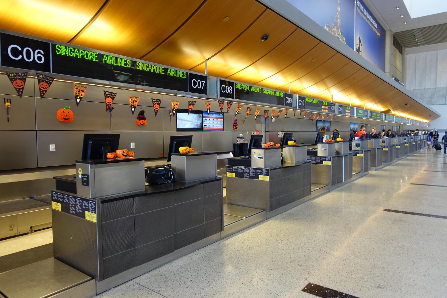 A long row of Singapore Airlines check-in counters at LAX, decorated with Halloween pumpkins and banners.