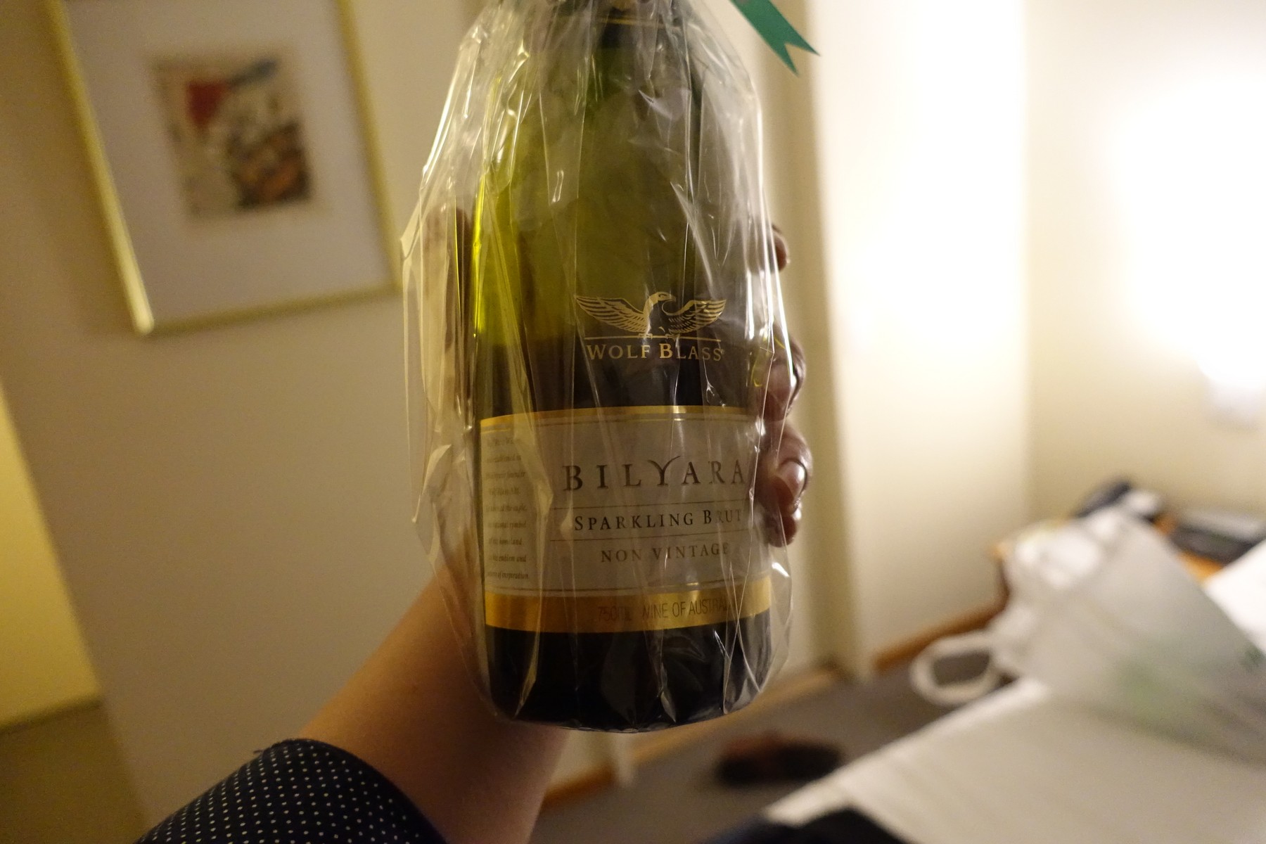 A hand holds a plastic-wrapped bottle of Wolf Blass Bilyara Sparkling Brut.