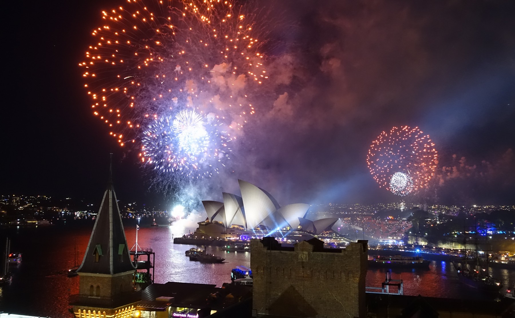 New Year's Eve fireworks explode over the illuminated Sydney Opera House and Harbour at night.
