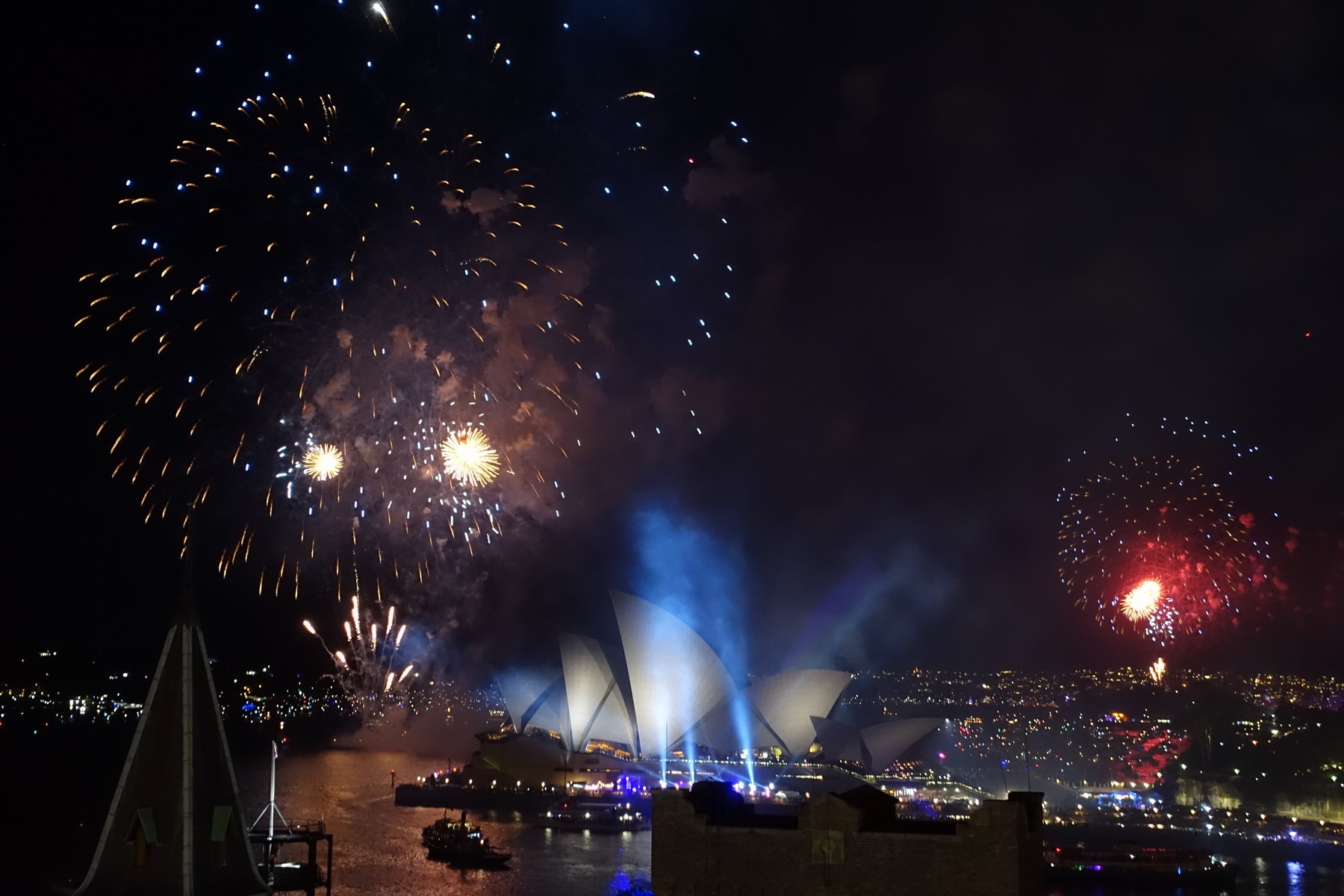 New Year's Eve fireworks explode over the Sydney Opera House and harbor at night.