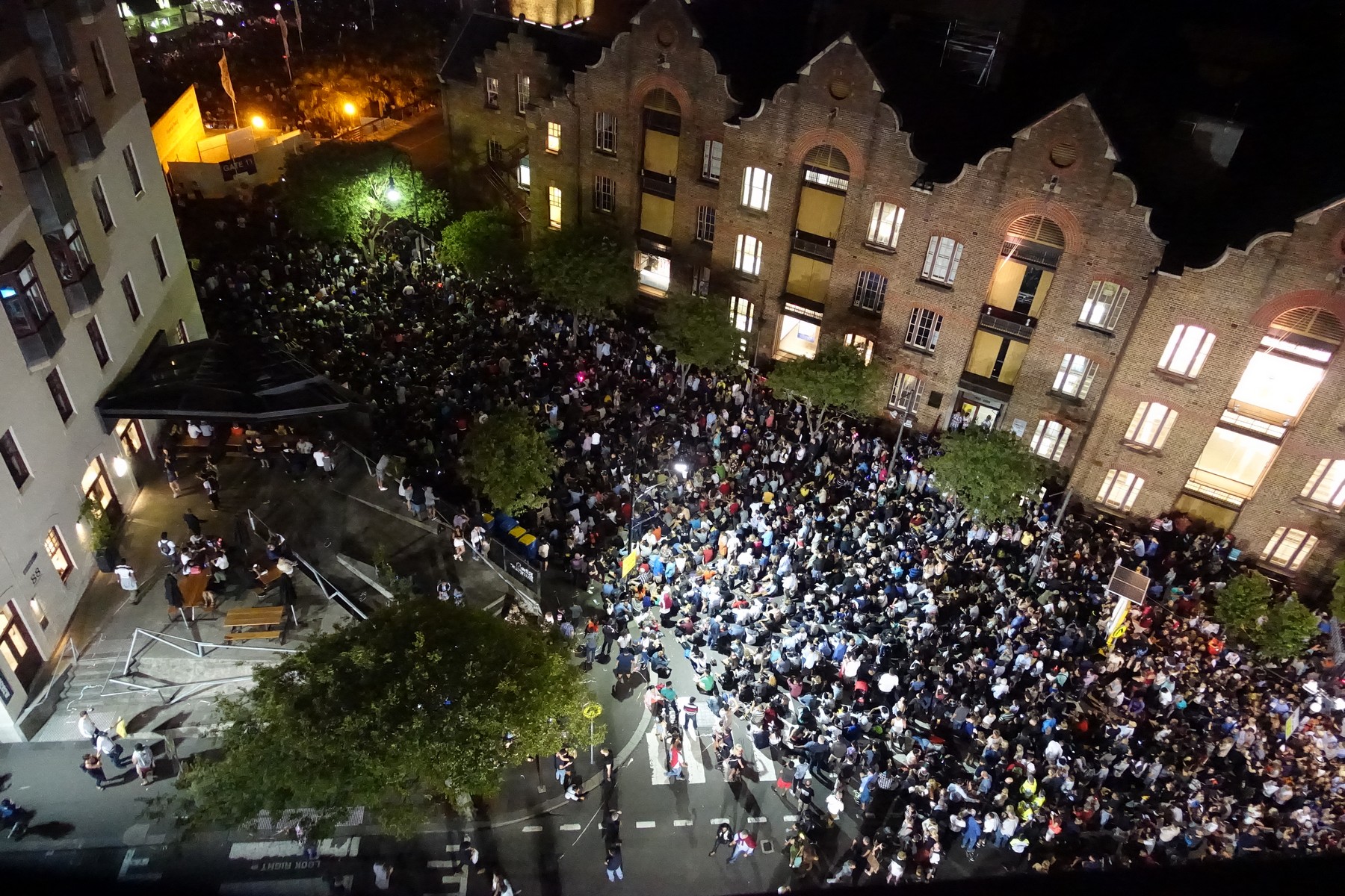 Nighttime aerial view of a street densely packed with people gathered for New Year's Eve.