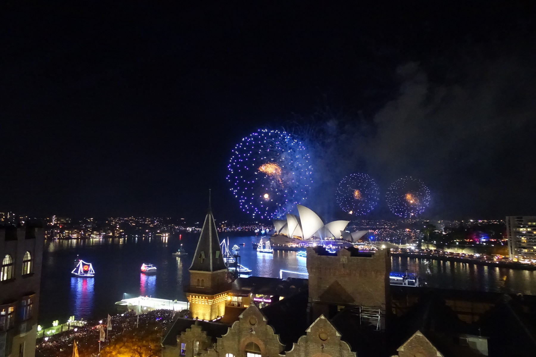 New Year's Eve fireworks erupt over the Sydney Opera House and illuminated boats on Sydney Harbour at night.