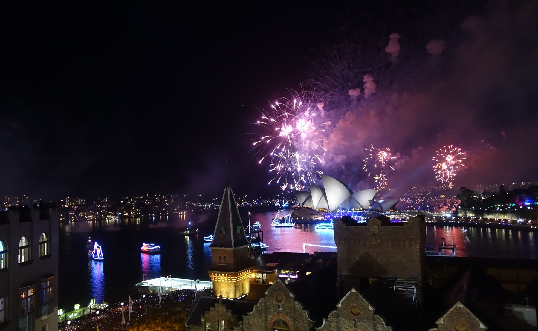 New Year's Eve fireworks in purple and pink illuminate the Sydney Opera House and Harbour at night.