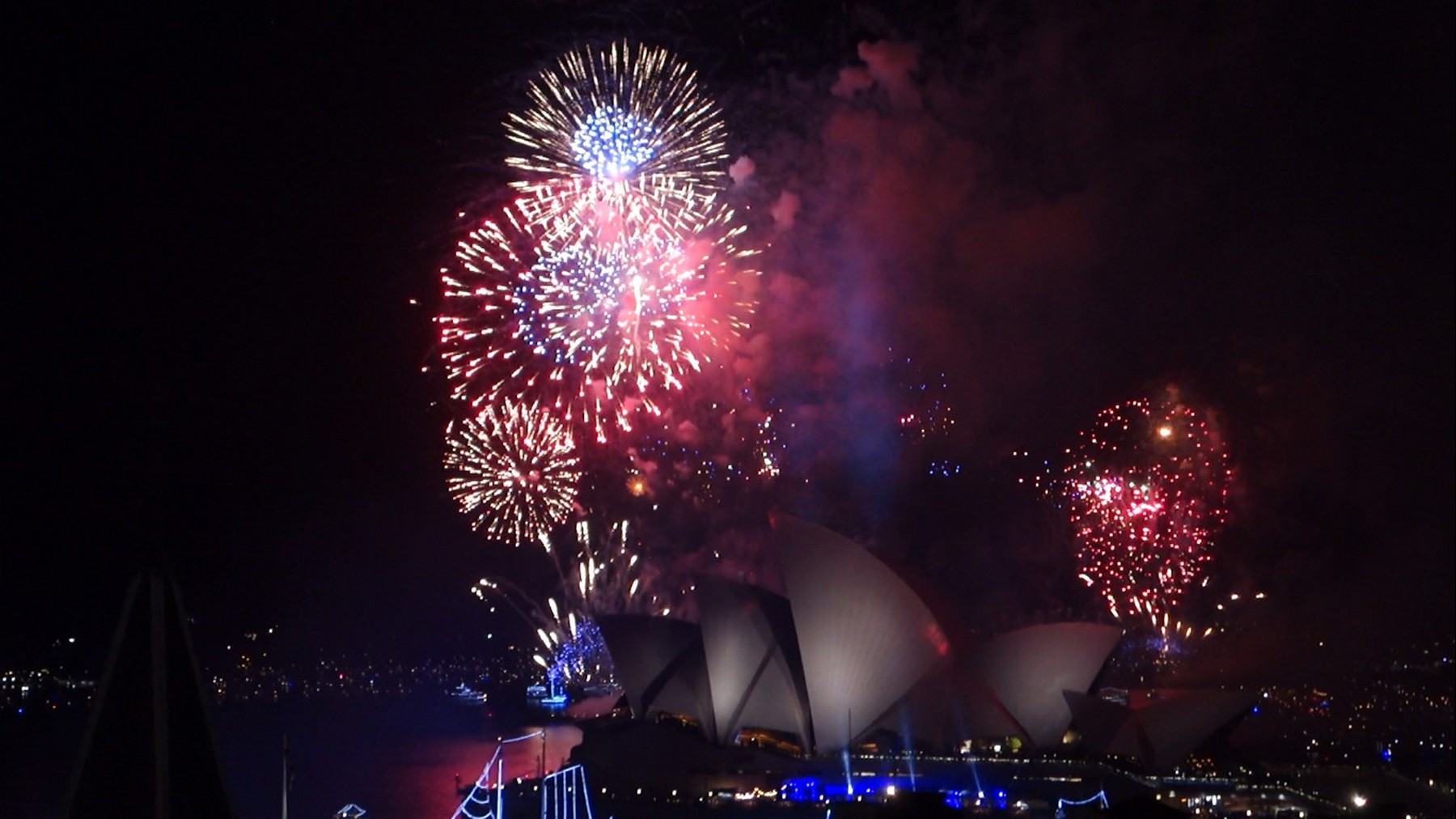 New Year's Eve fireworks illuminate the Sydney Opera House and harbor at night.