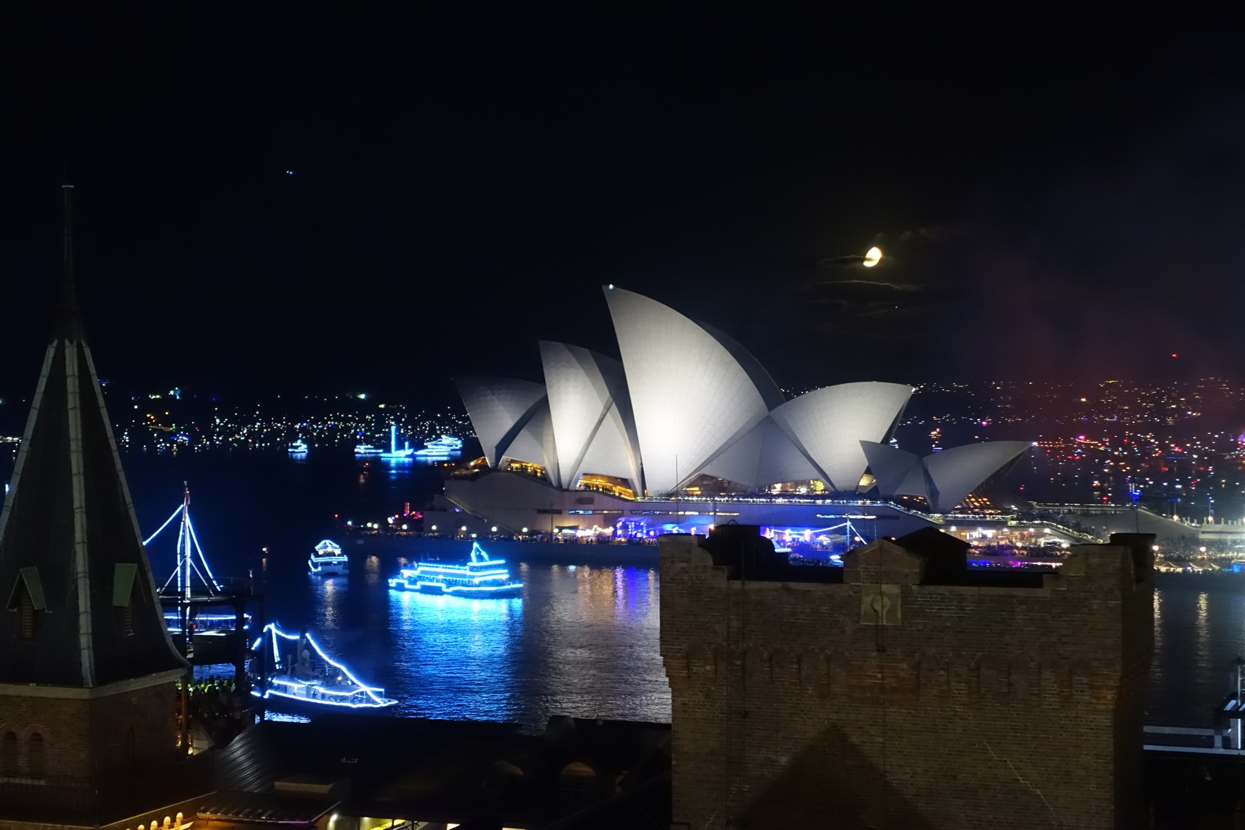 Sydney Opera House illuminated at night, with festive boats on the harbour during New Year's Eve.