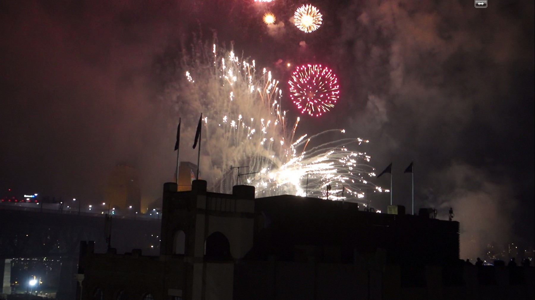 New Year's Eve fireworks burst over a dark building in Sydney at night.