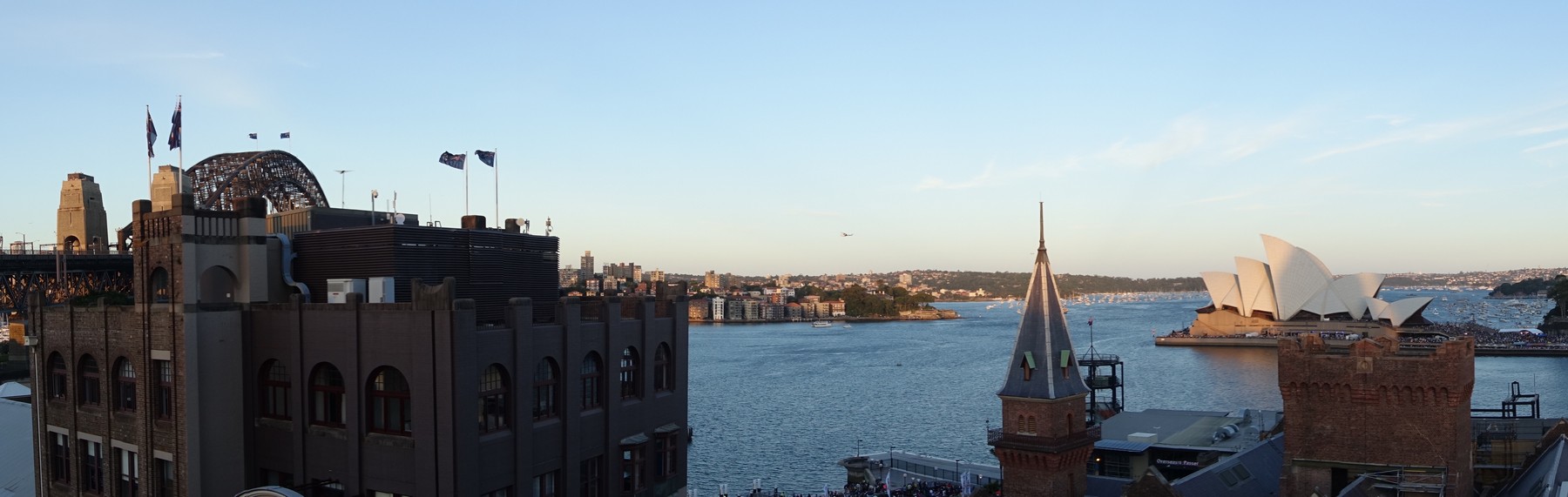 A panoramic view of Sydney Harbour featuring the Harbour Bridge, Opera House, and numerous boats on the water.