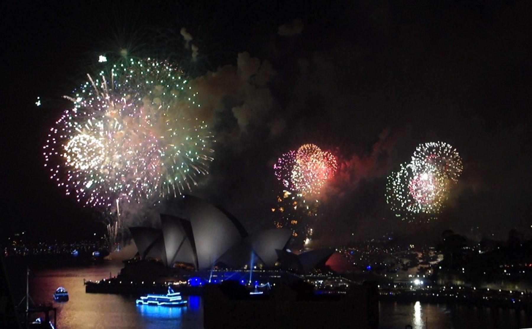 New Year's Eve fireworks explode above the Sydney Opera House and harbor at night.