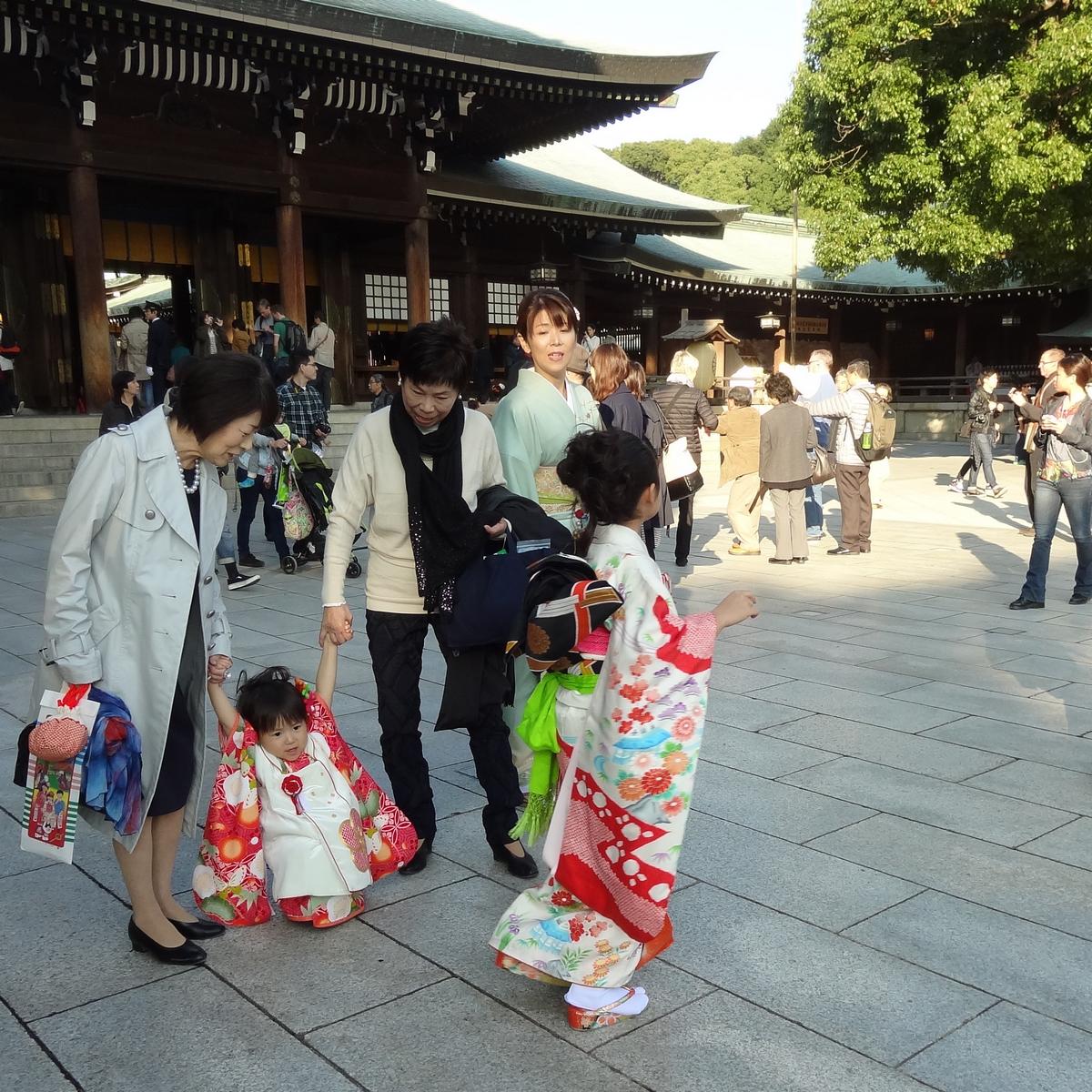 Two young girls in colorful kimonos with adults in a Japanese temple courtyard.