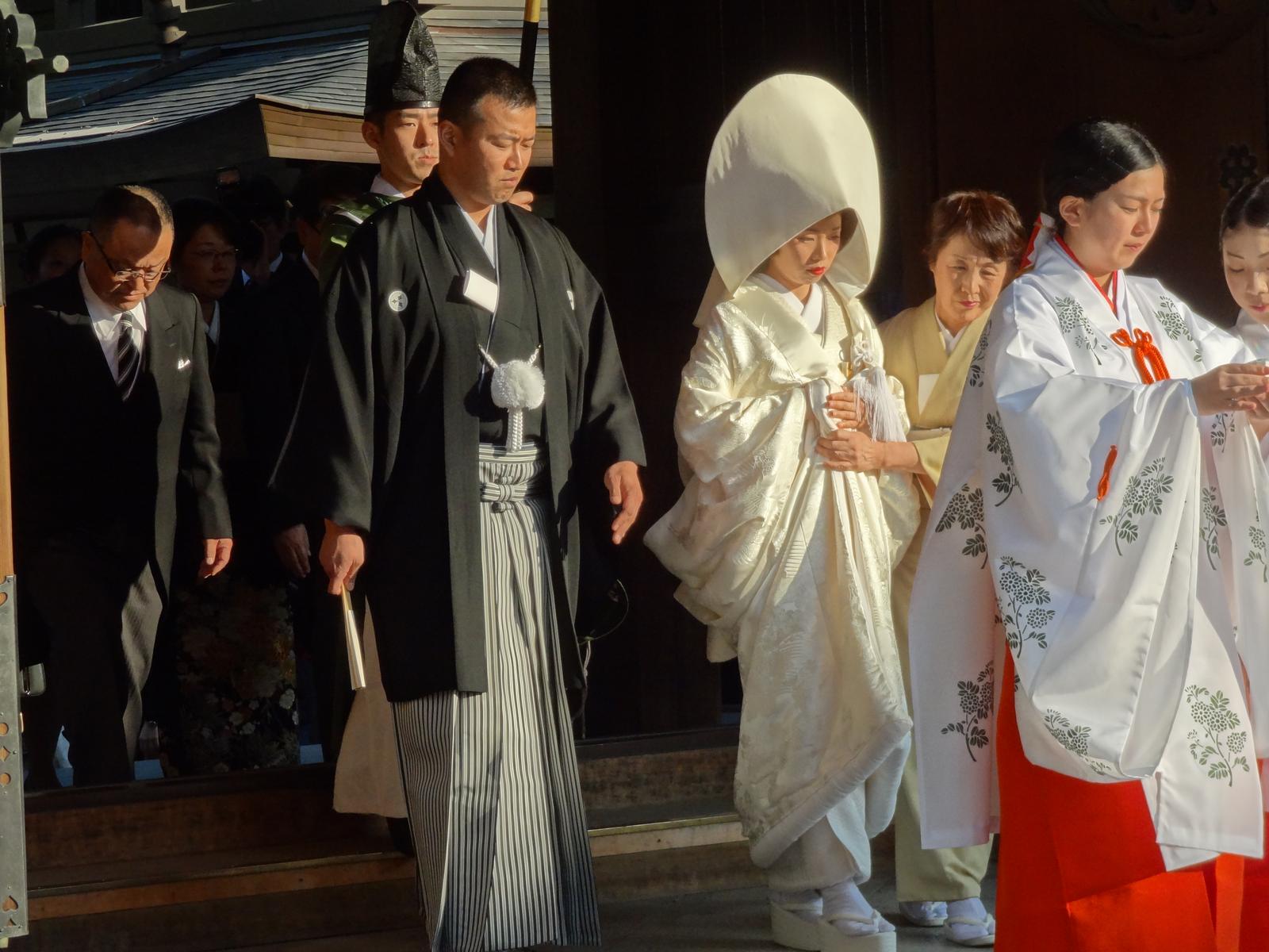 A traditional Japanese wedding ceremony featuring a bride in a white kimono with a large white hood and a groom in a black kimono.