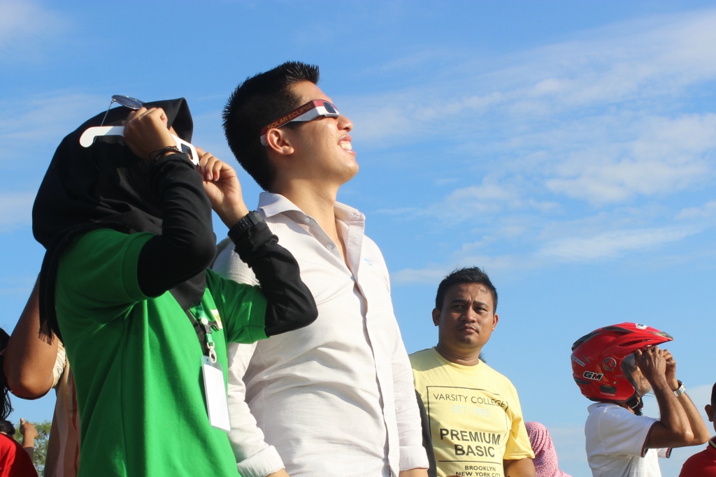 Spectators look skyward, some wearing eclipse glasses, during a total solar eclipse.