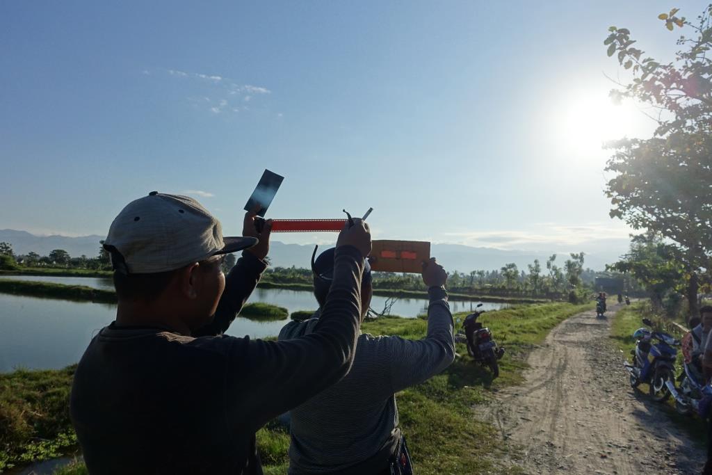 Two people hold up improvised filters and viewers to look at the bright sun.