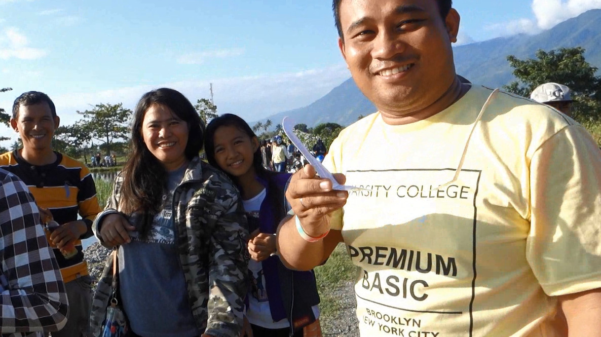 A group of smiling people in Palu, Indonesia, with one man holding a white eclipse viewing device.