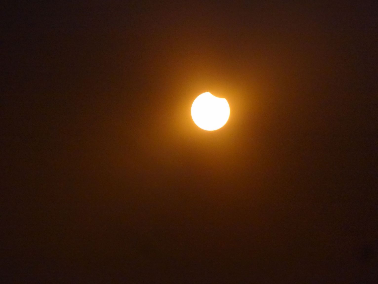 A partial solar eclipse shows a bright sun with a dark crescent shape on its top right.