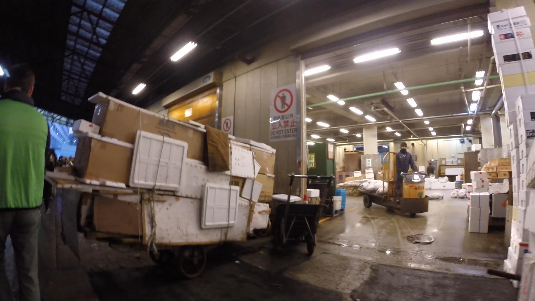 Workers transport boxes and containers on carts inside the bustling Tsukiji Fish Market.