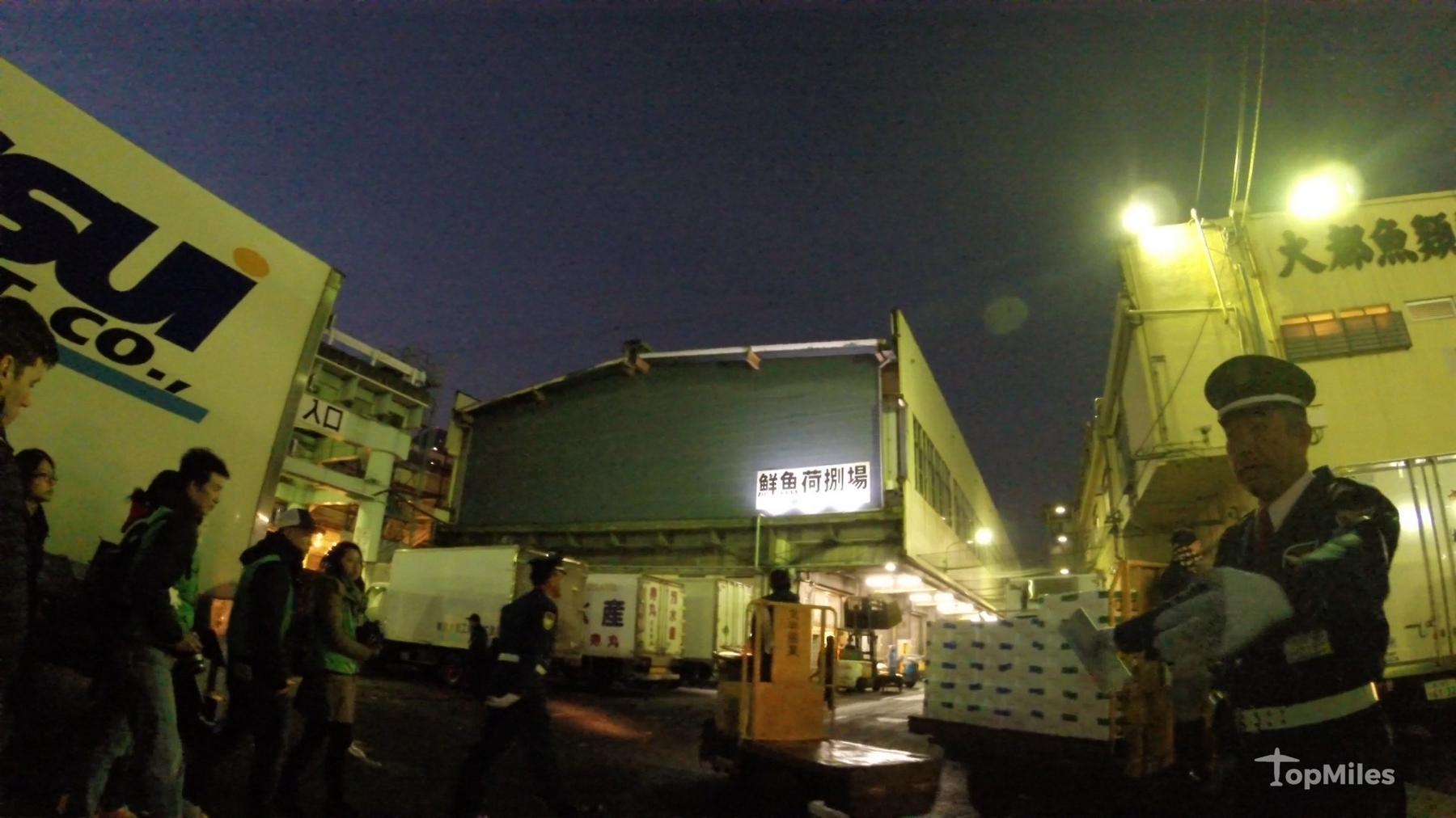Early morning at Tsukiji Fish Market with a uniformed guard and a "Fresh Fish Unloading Area" sign.