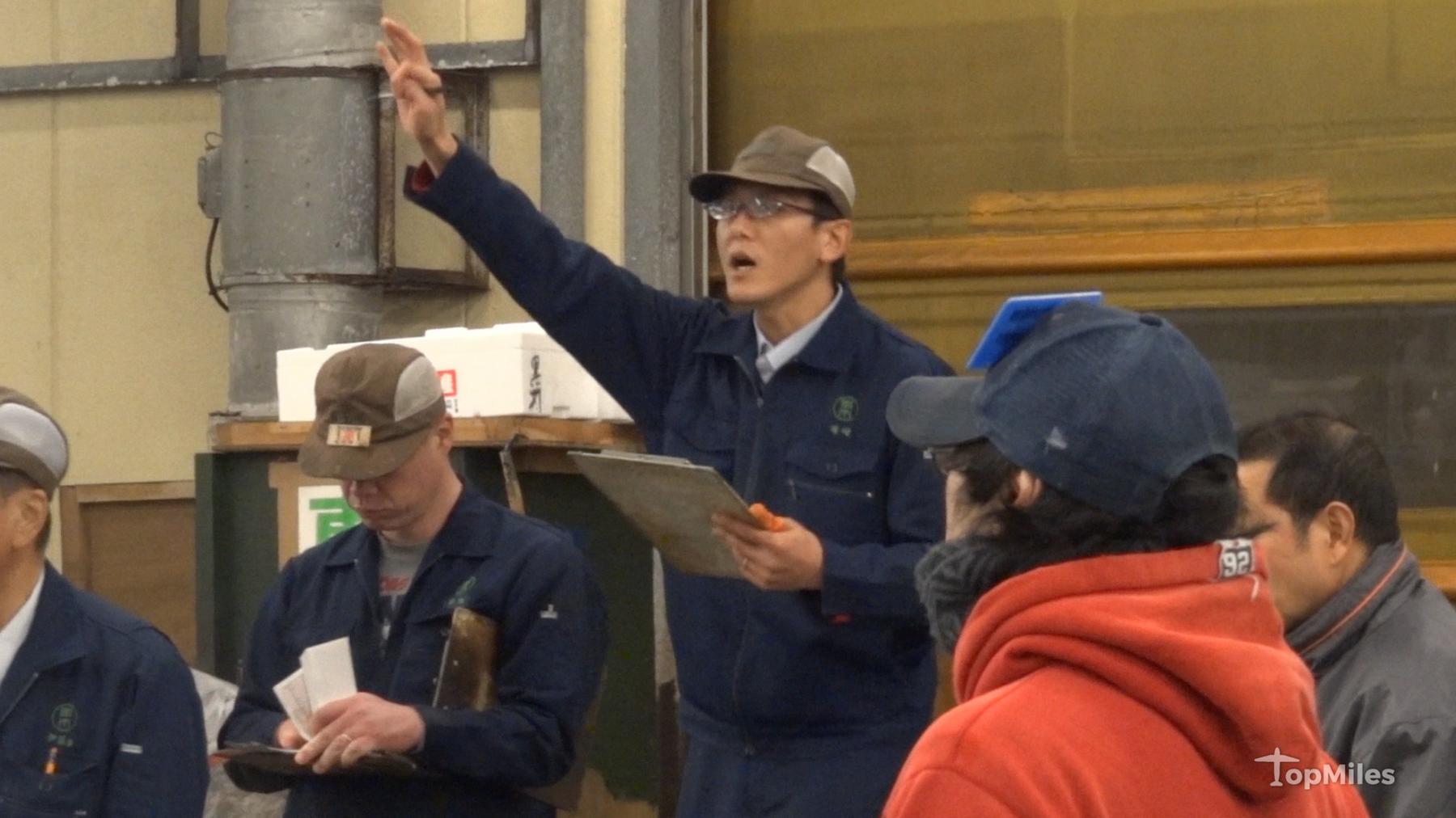 An auctioneer raises his hand and calls bids at the Tsukiji tuna auction.